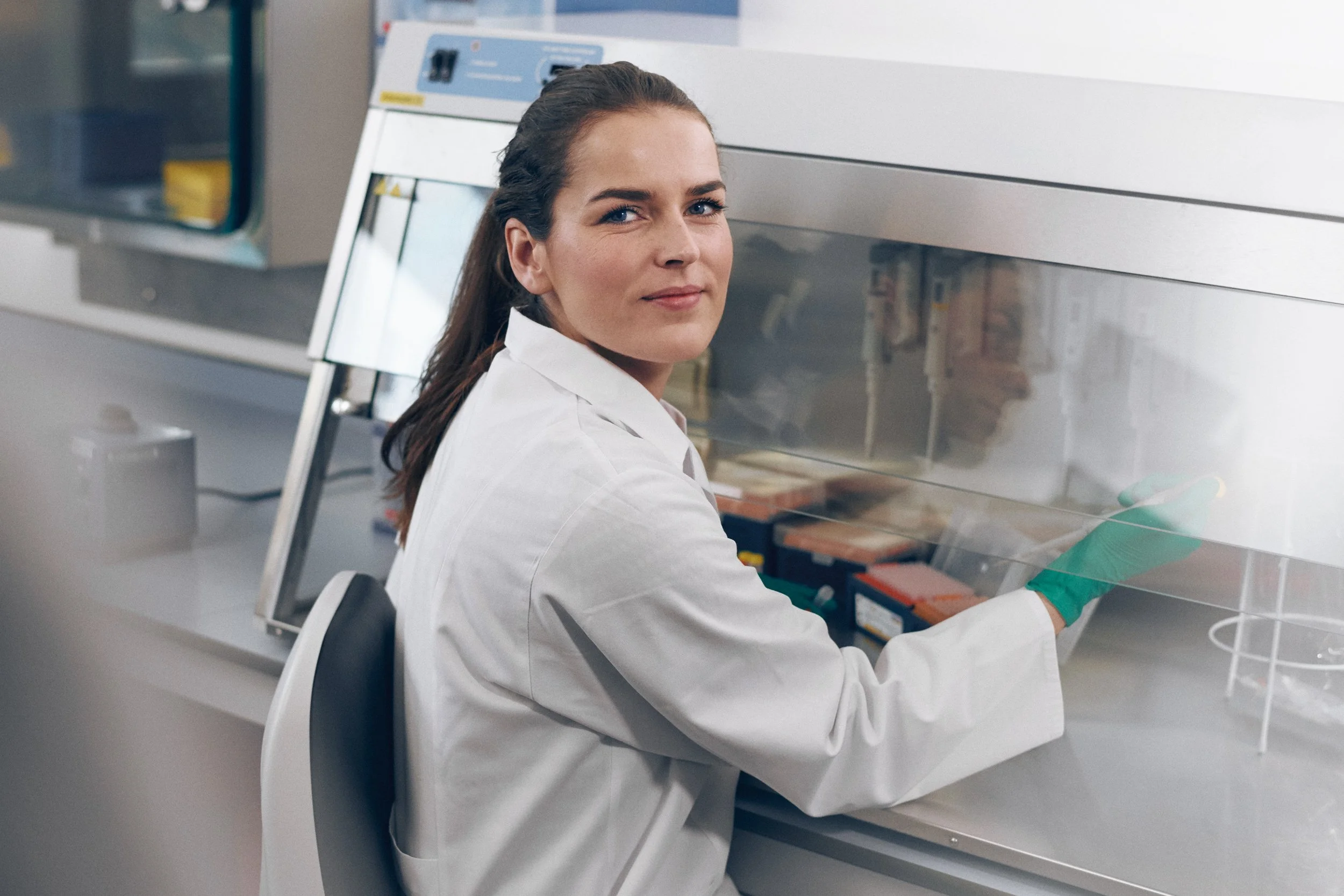 Laboratory technician handling samples inside biosafety cabinet, controlled analysis environment