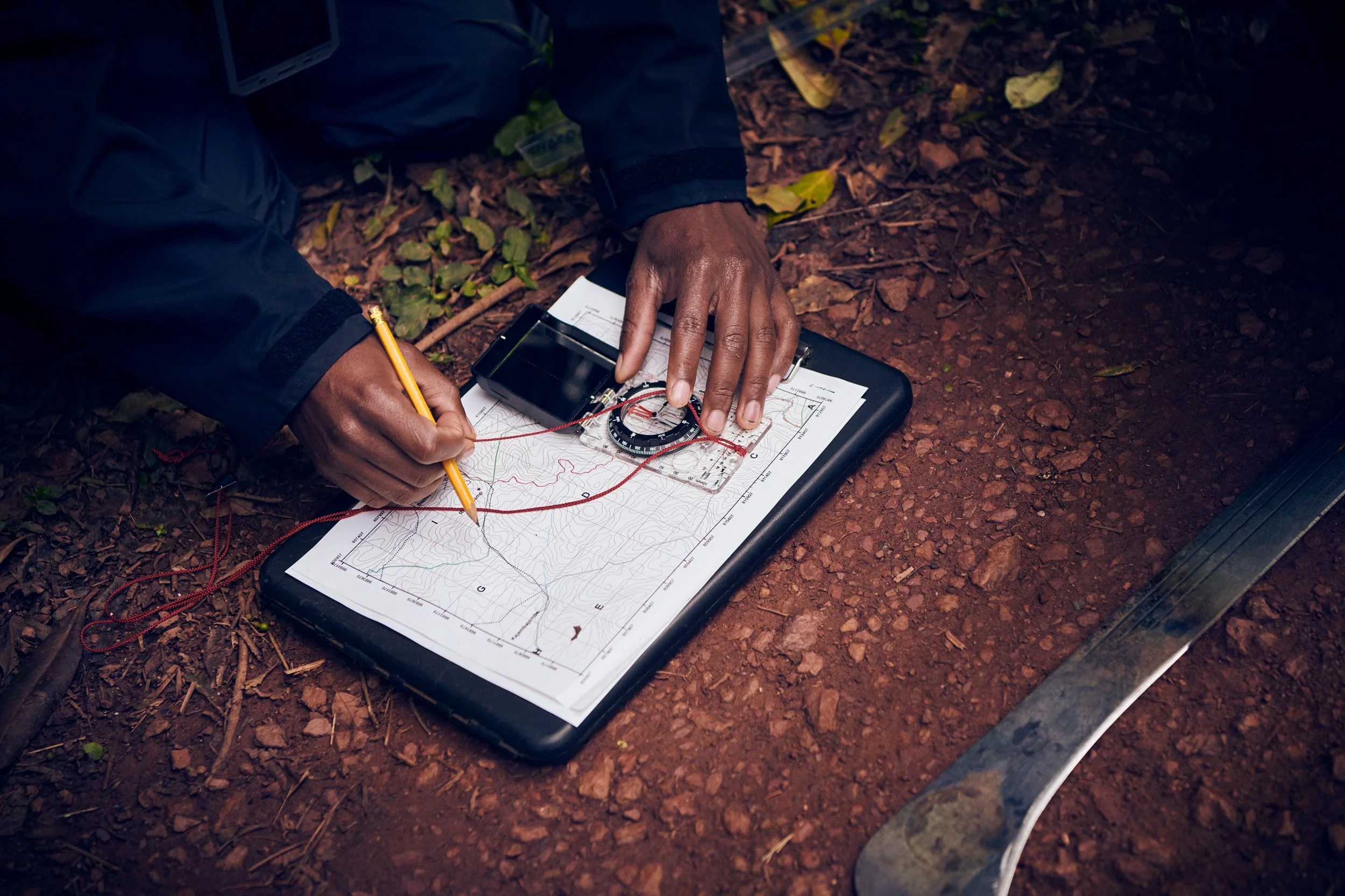 Hands marking route on map with compass, navigation detail in field conditions