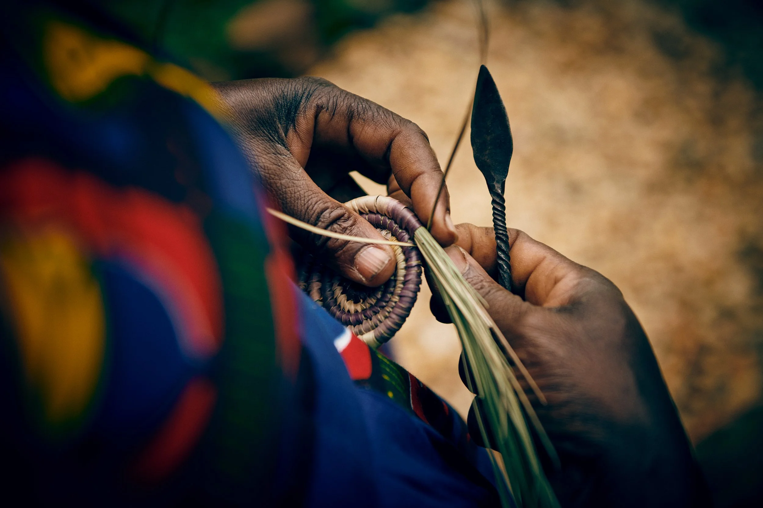 Hands weaving natural fibres into basket, detailed craft process