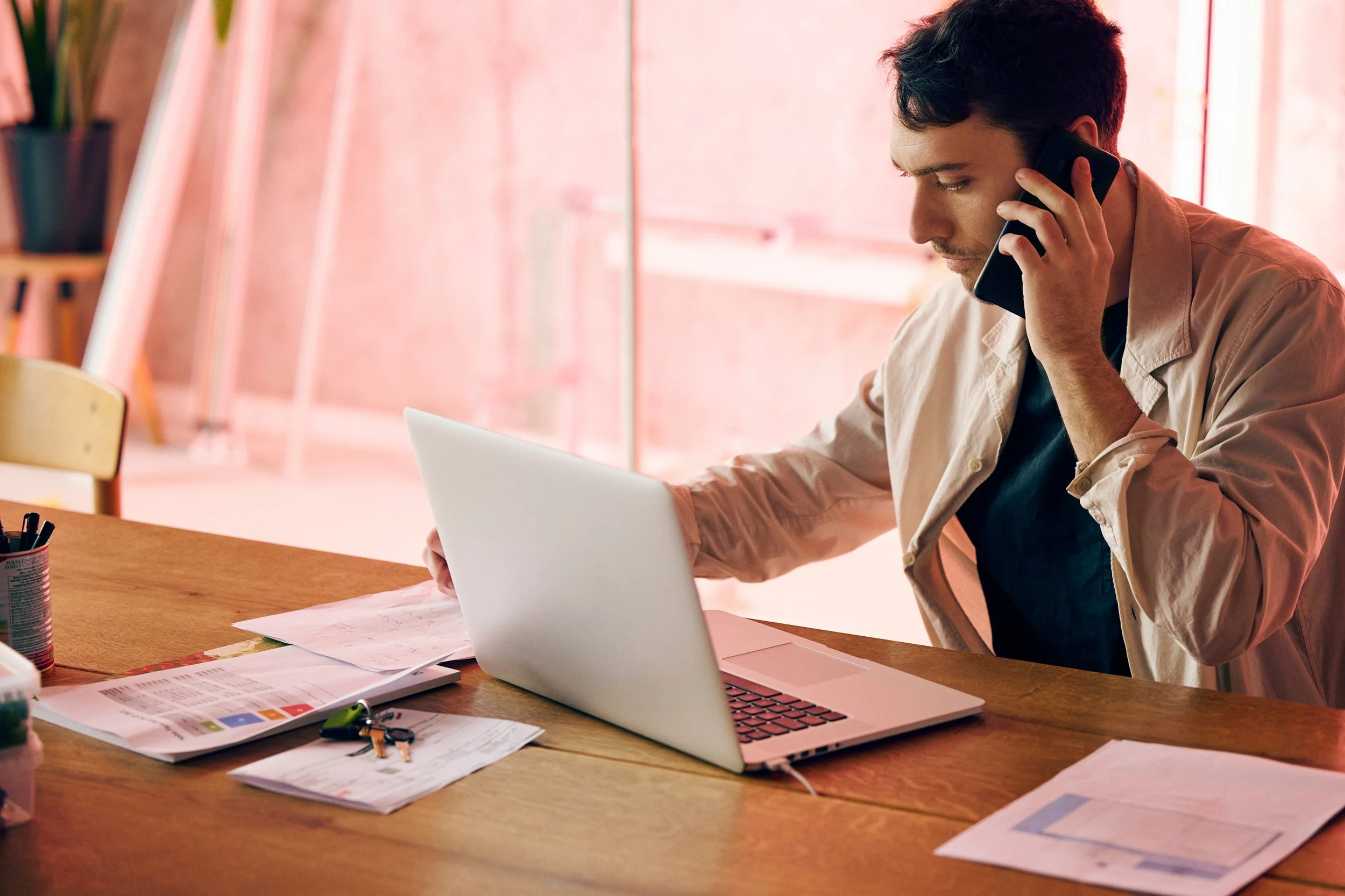 Man working on laptop at home while on phone