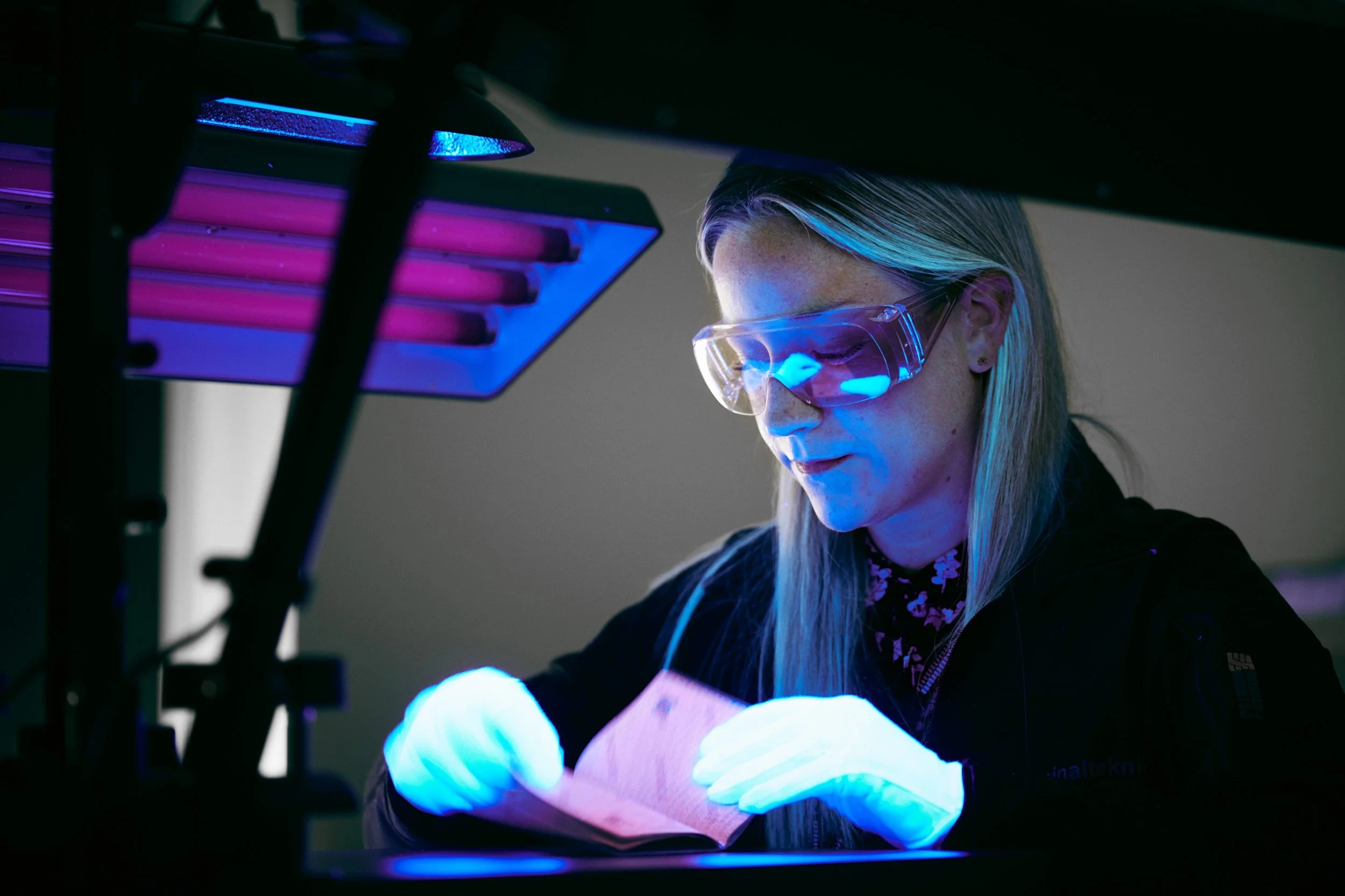 Technician working under UV light inspecting material in laboratory