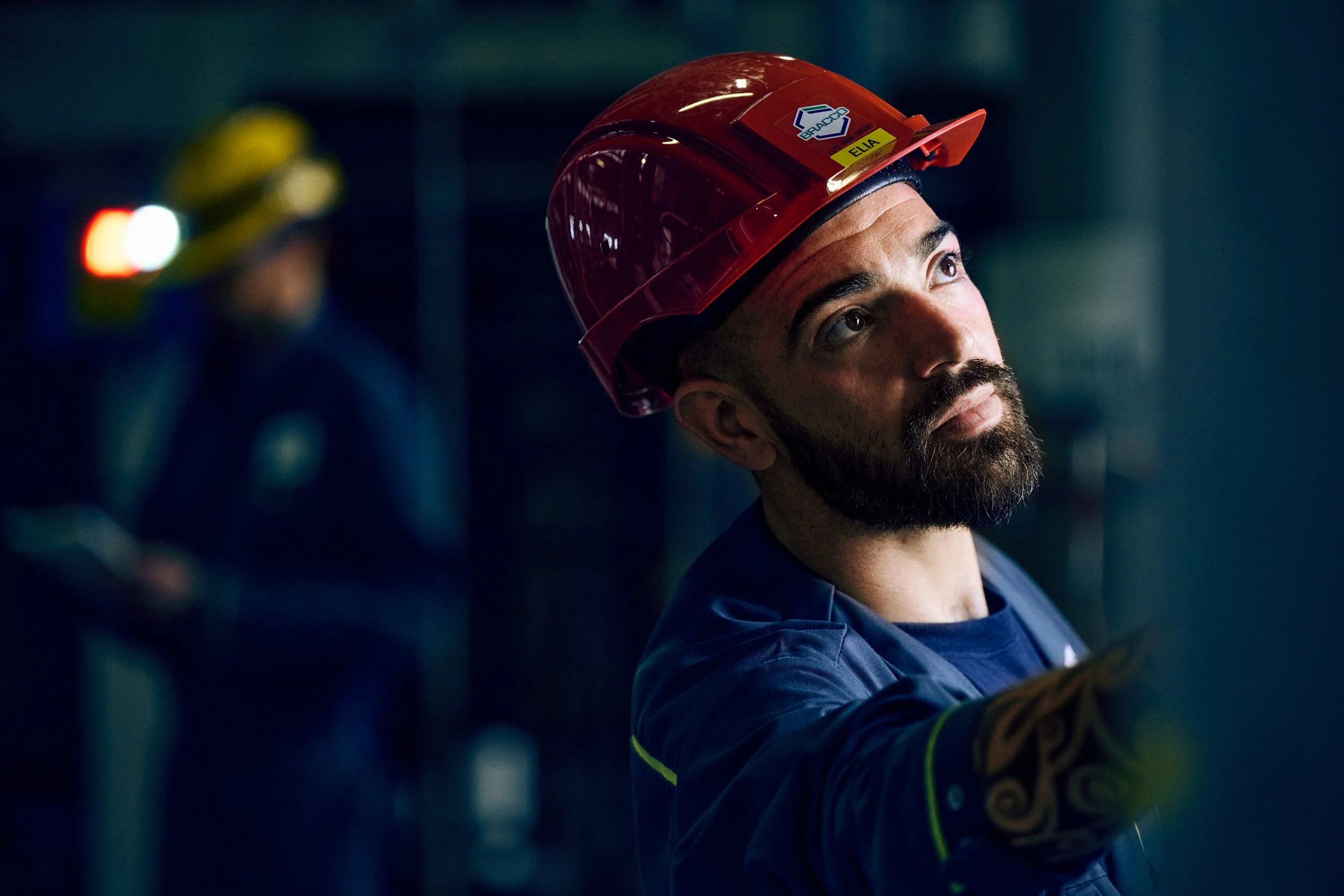 Technician in safety helmet looking upward while operating equipment, active production task