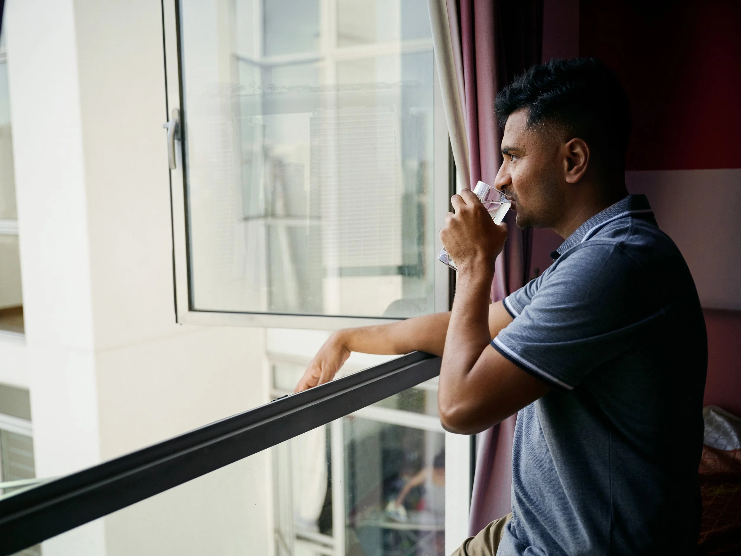 Man drinking water while standing by window in apartment