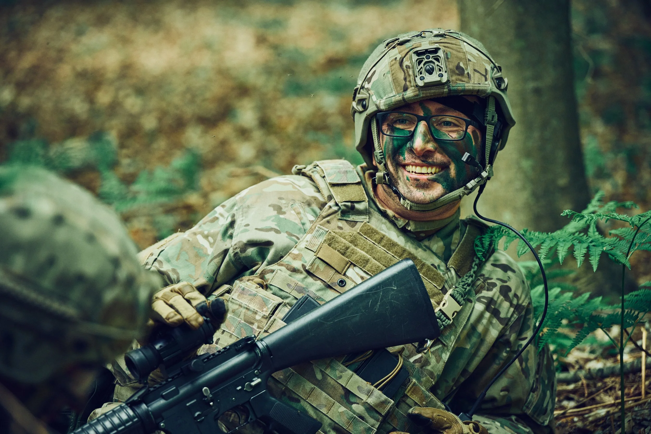 Smiling soldier in camouflage resting with rifle during field exercise in forest
