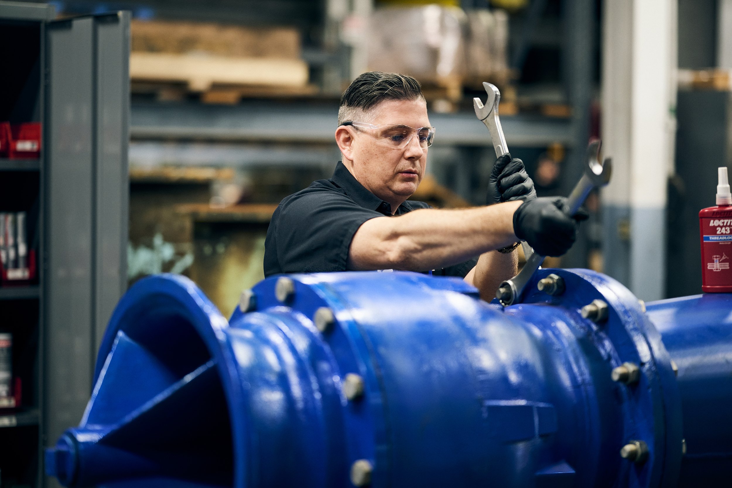 Technician tightening bolts on large blue industrial pump system