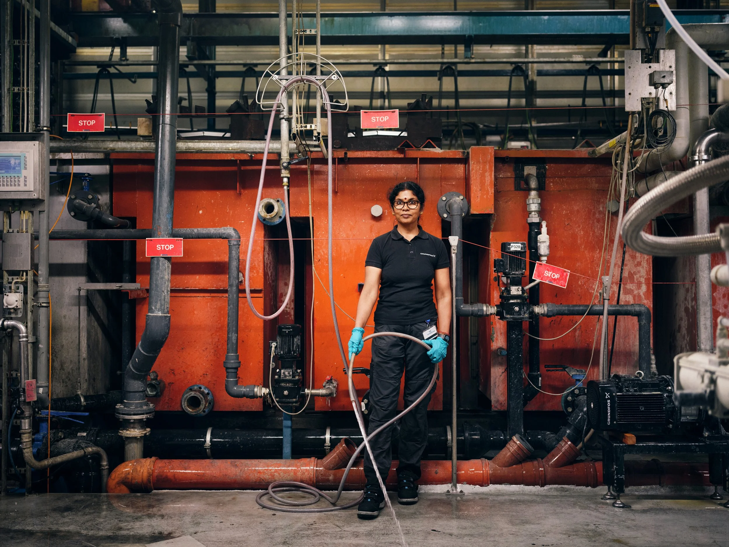 Technician standing in front of industrial piping system holding hose in production environment
