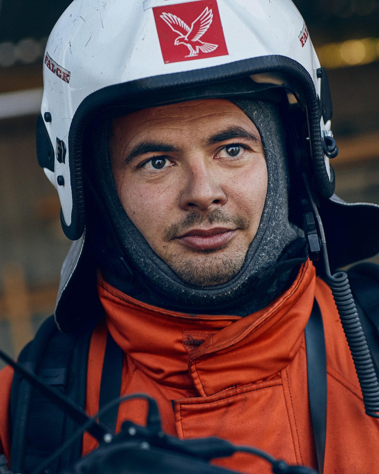 Close-up of a man wearing a white helmet with an eagle logo, a black inner helmet lining, and an orange jacket, outdoors.