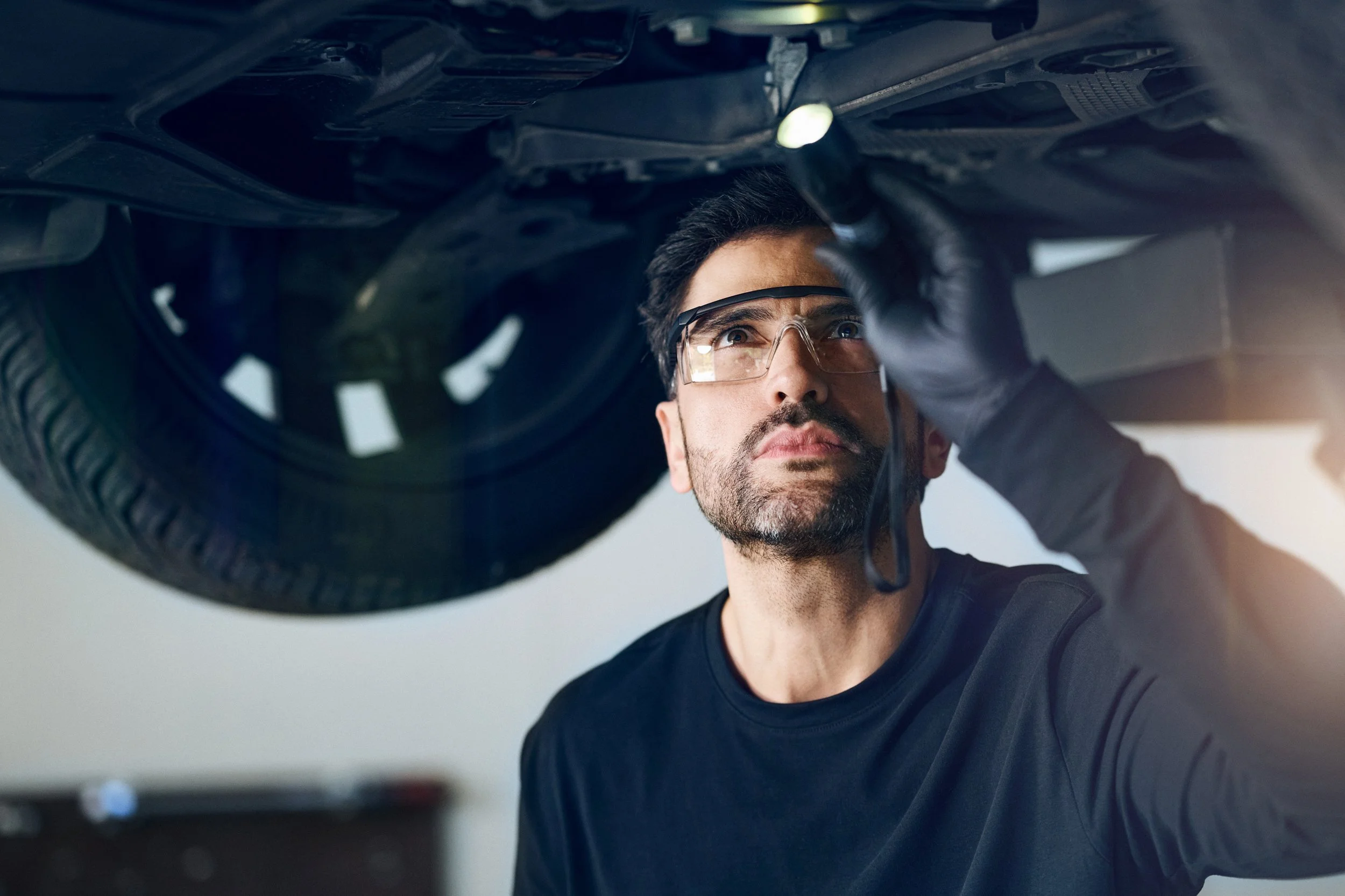 Mechanic inspecting underside of car on lift, focused technical task