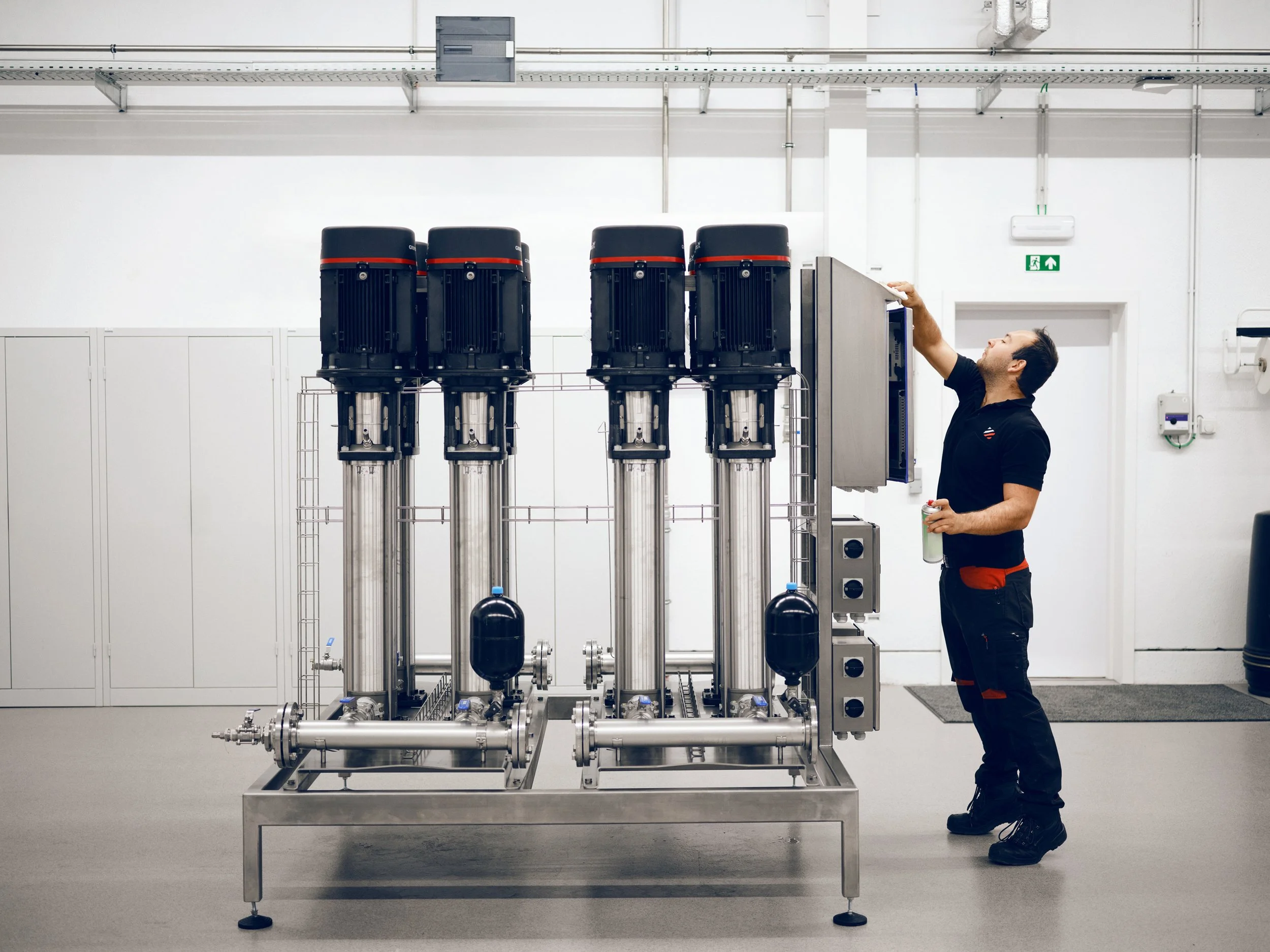 Technician cleaning control cabinet beside vertical pump system