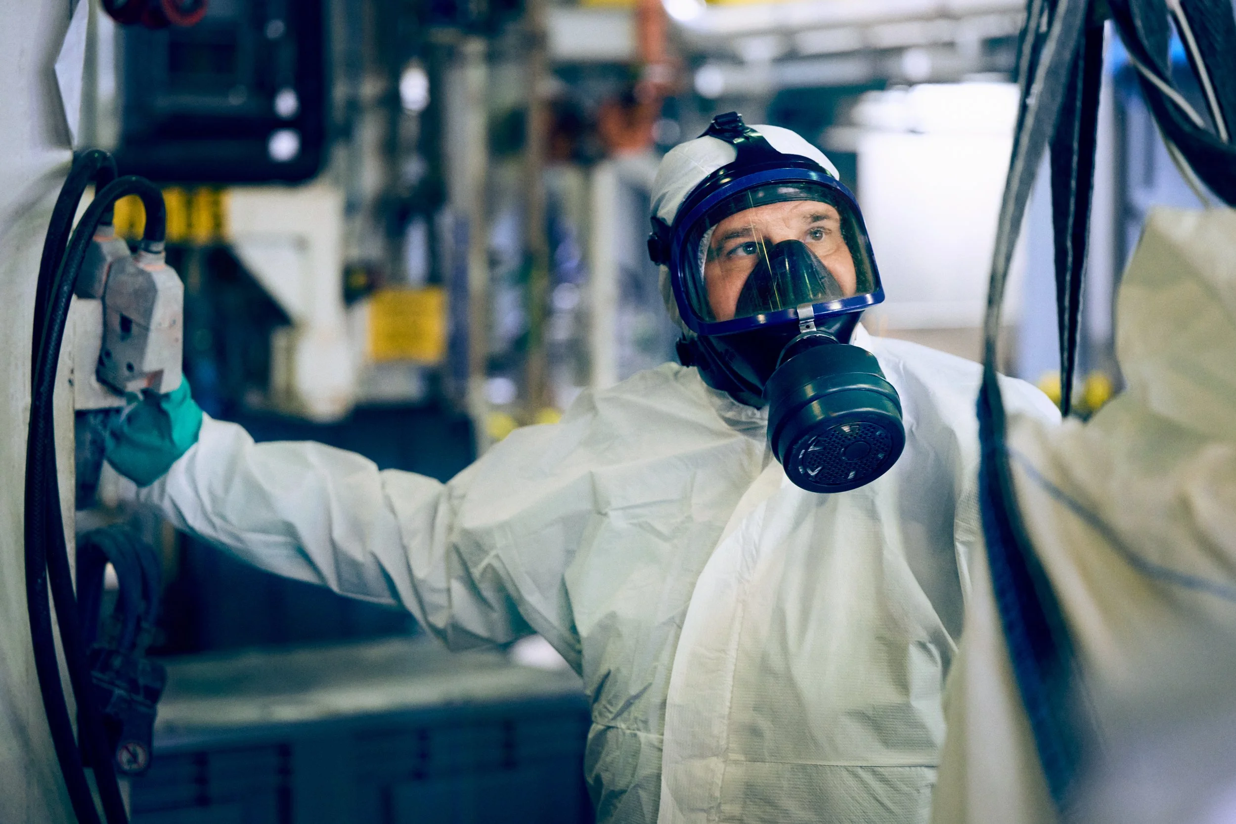 Worker in protective suit and respirator operating equipment in controlled production area