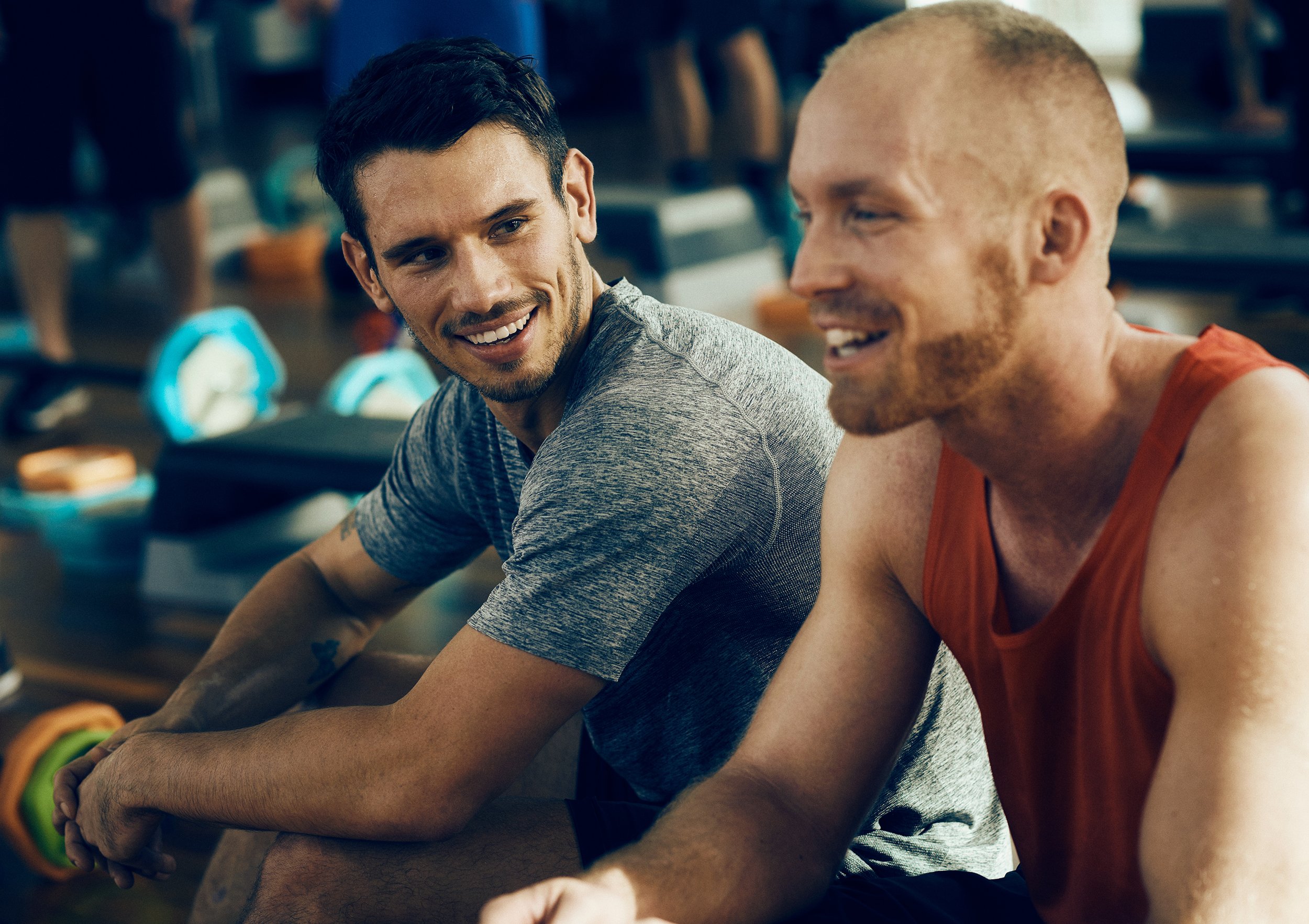 Two men resting between sets in gym, social training moment
