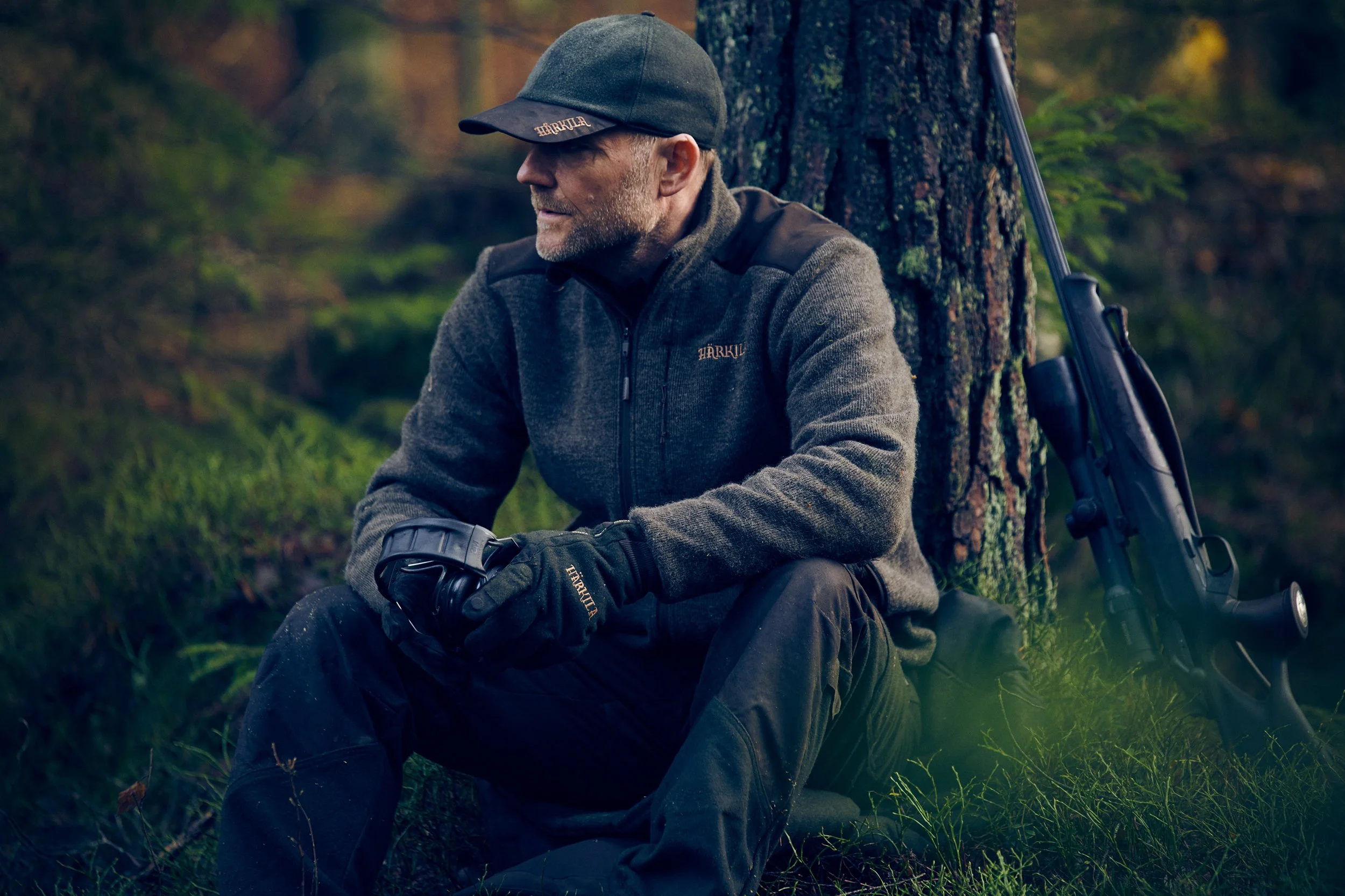 Hunter seated against tree in forest, resting moment in natural environment