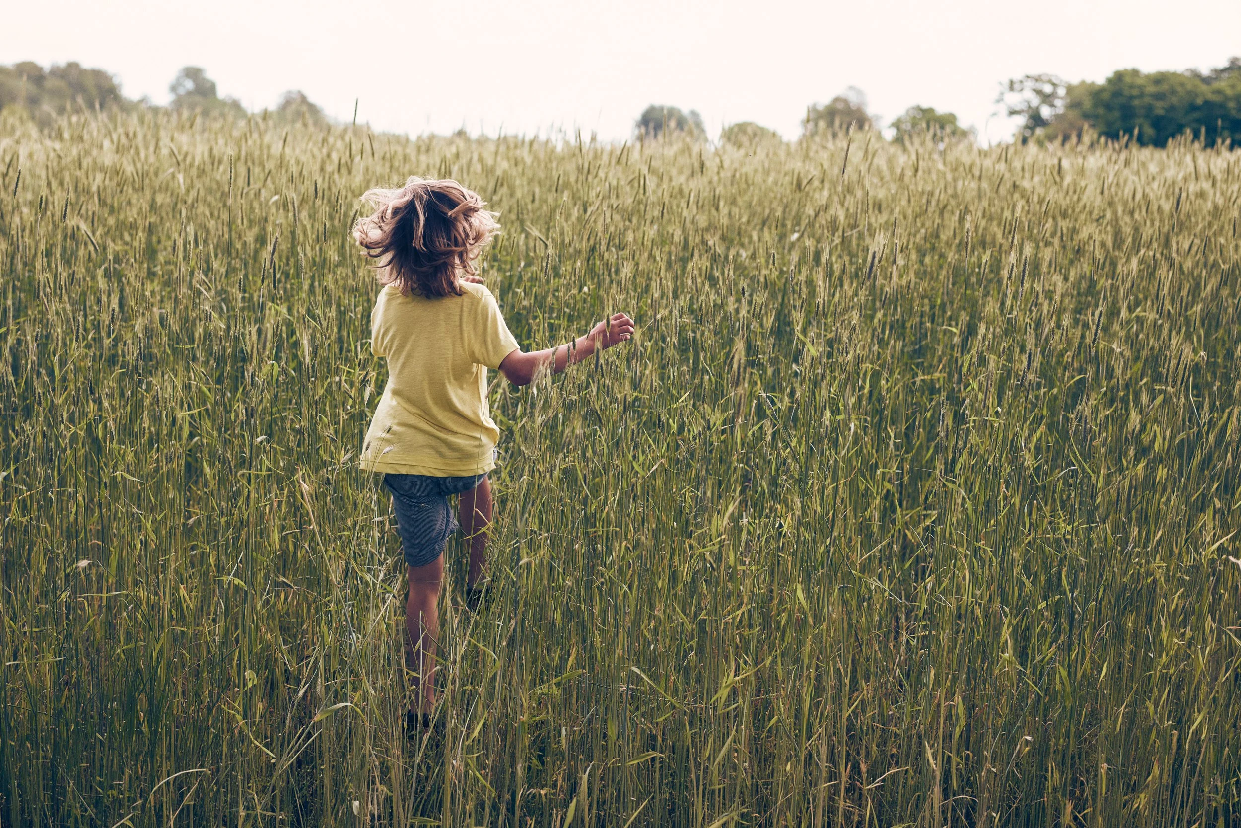 Child running through tall grass field, summer movement