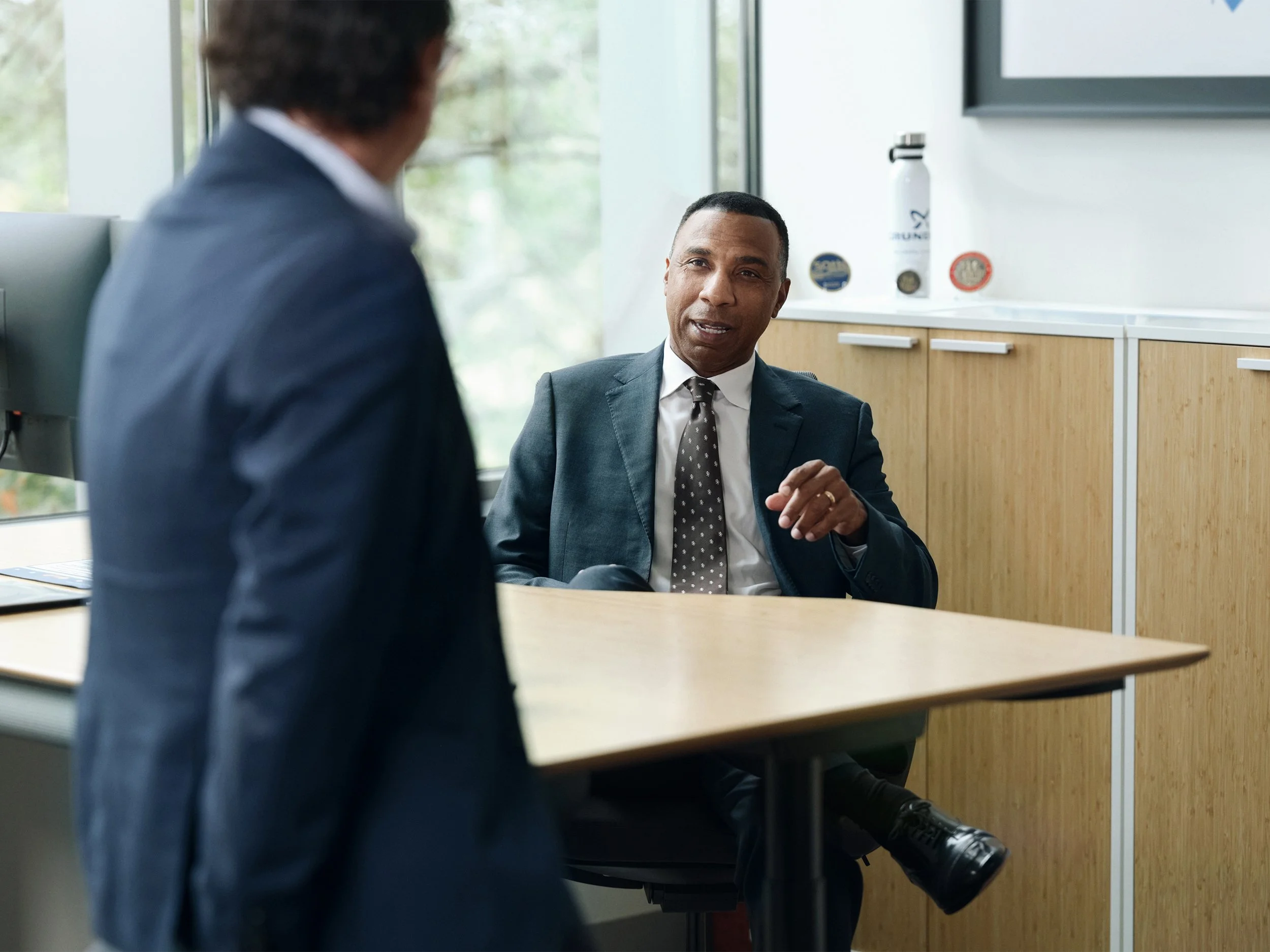 Business meeting between two professionals in office, CEO seated at desk in suit