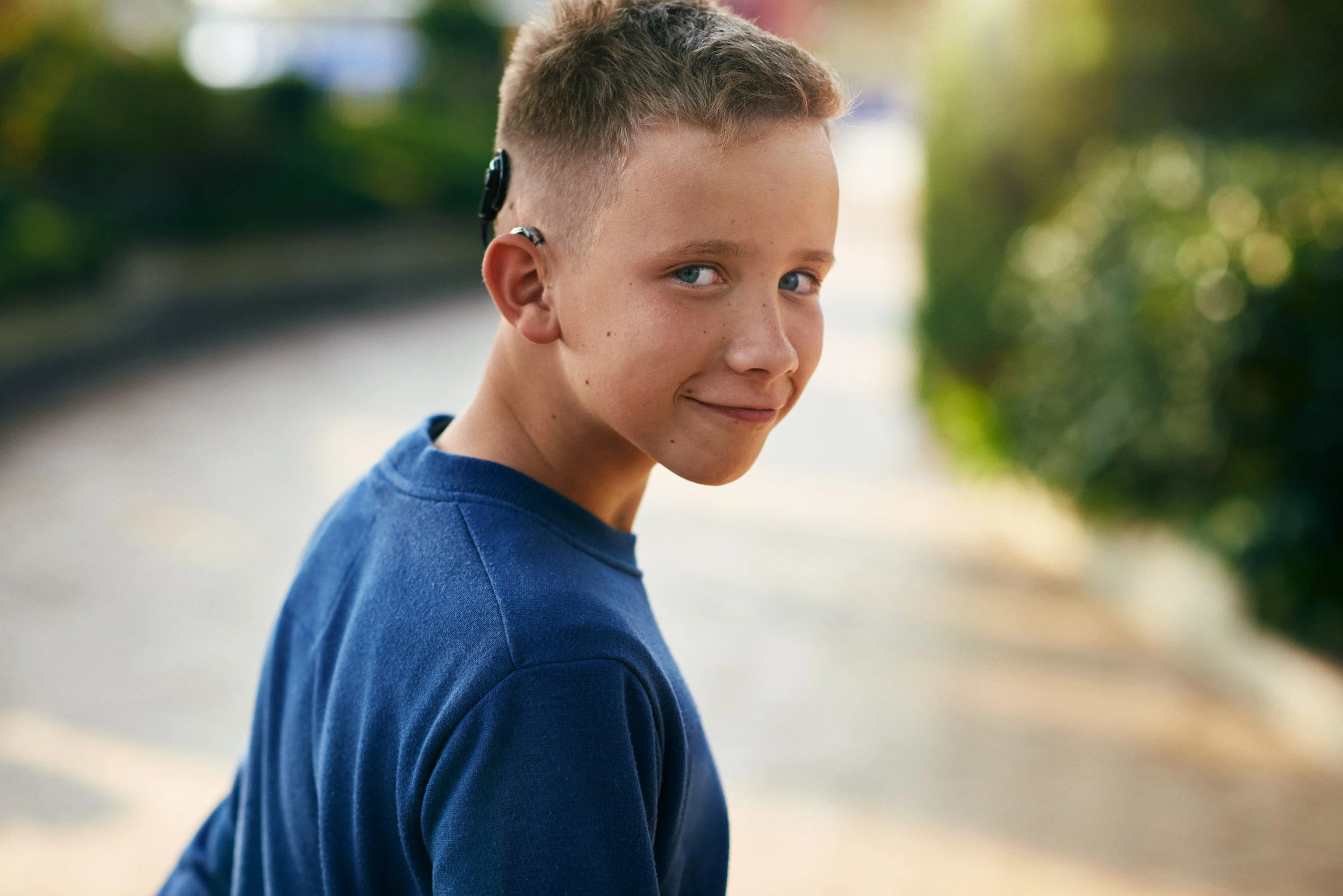 Boy wearing cochlear implant looking back while walking outdoors, natural everyday moment