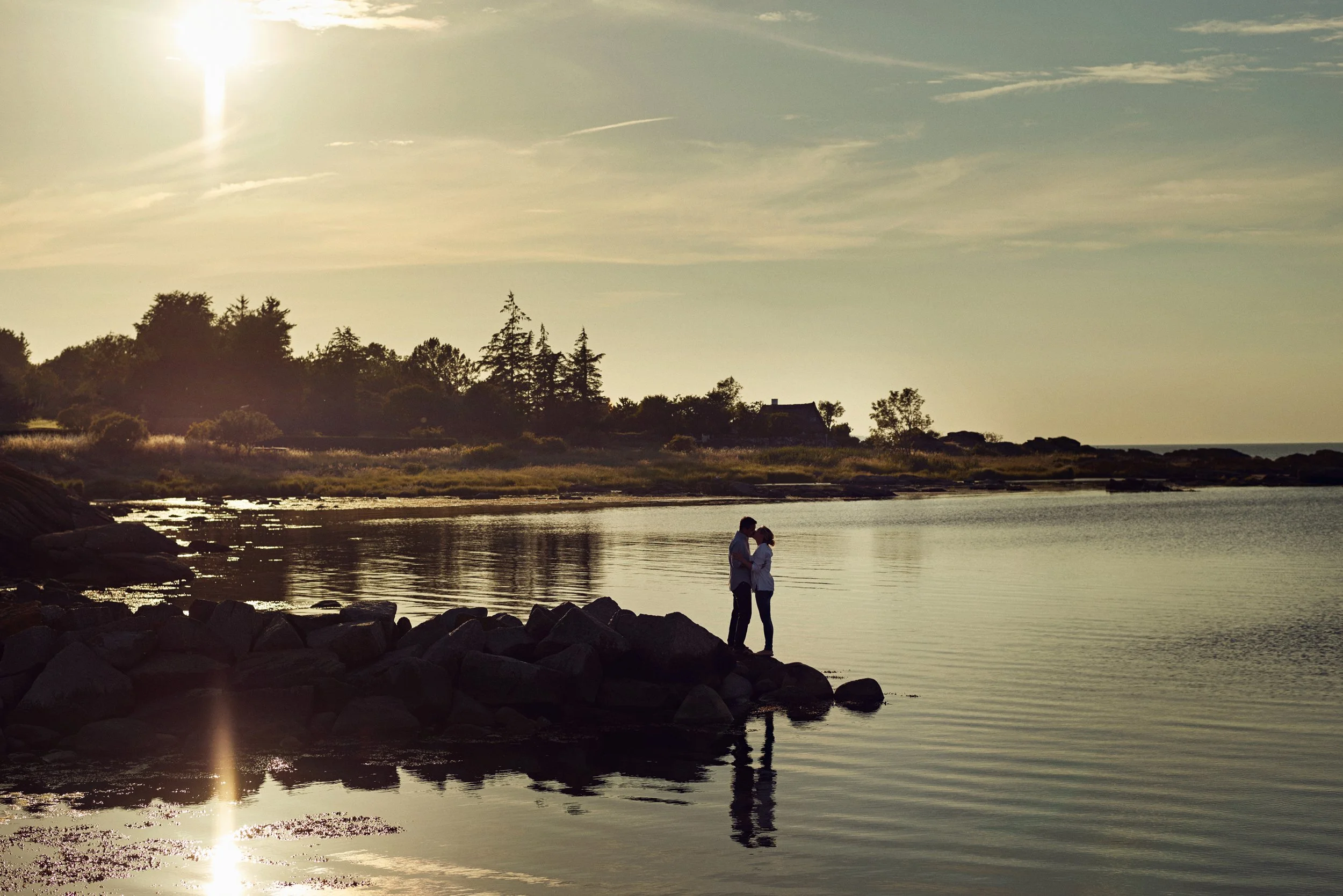 Couple standing on rocks by calm water at sunset, quiet end-of-day moment