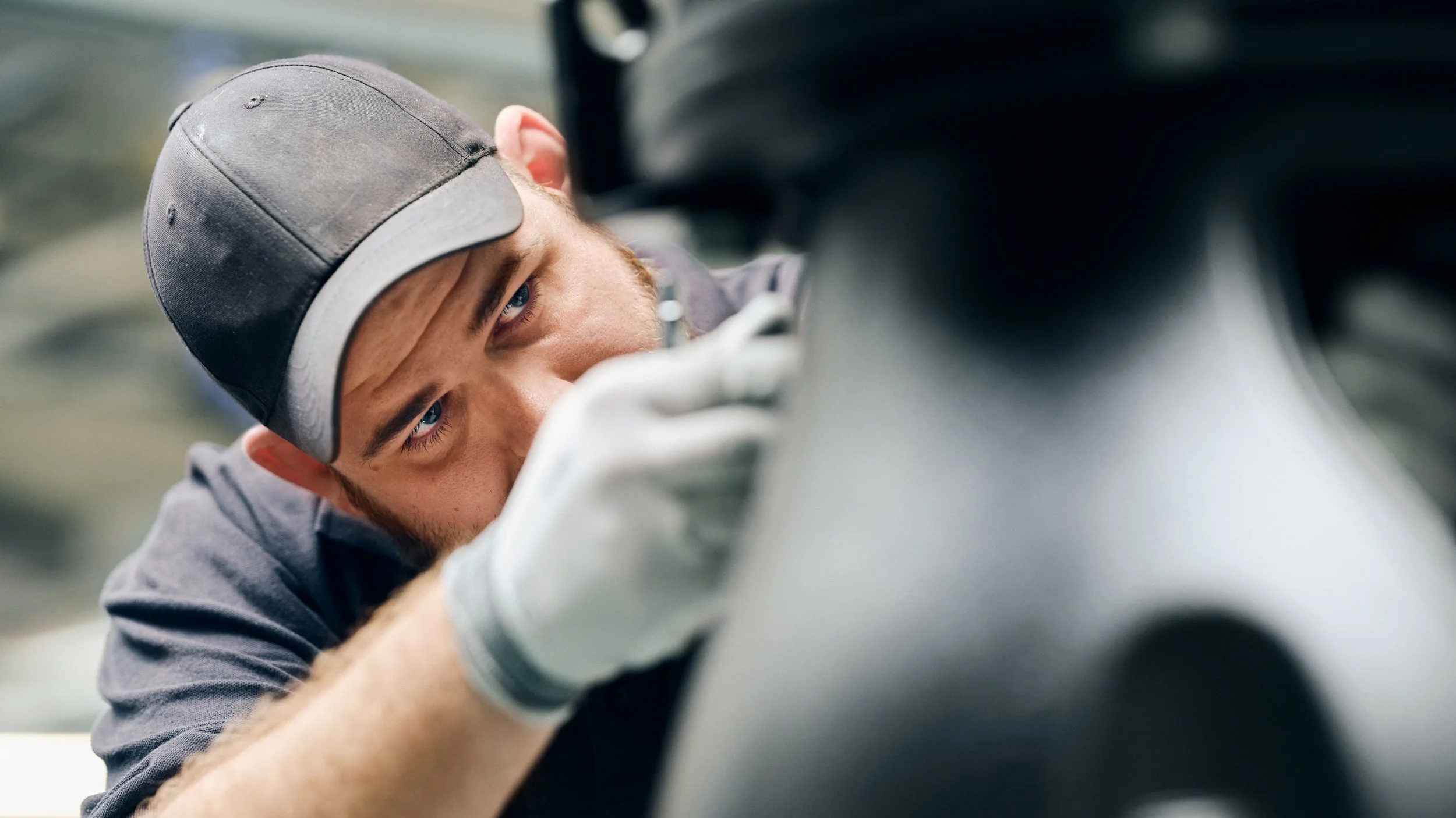 A young man wearing a gray baseball cap and gray work gloves, focused intently on a task, possibly mechanical or repair work.