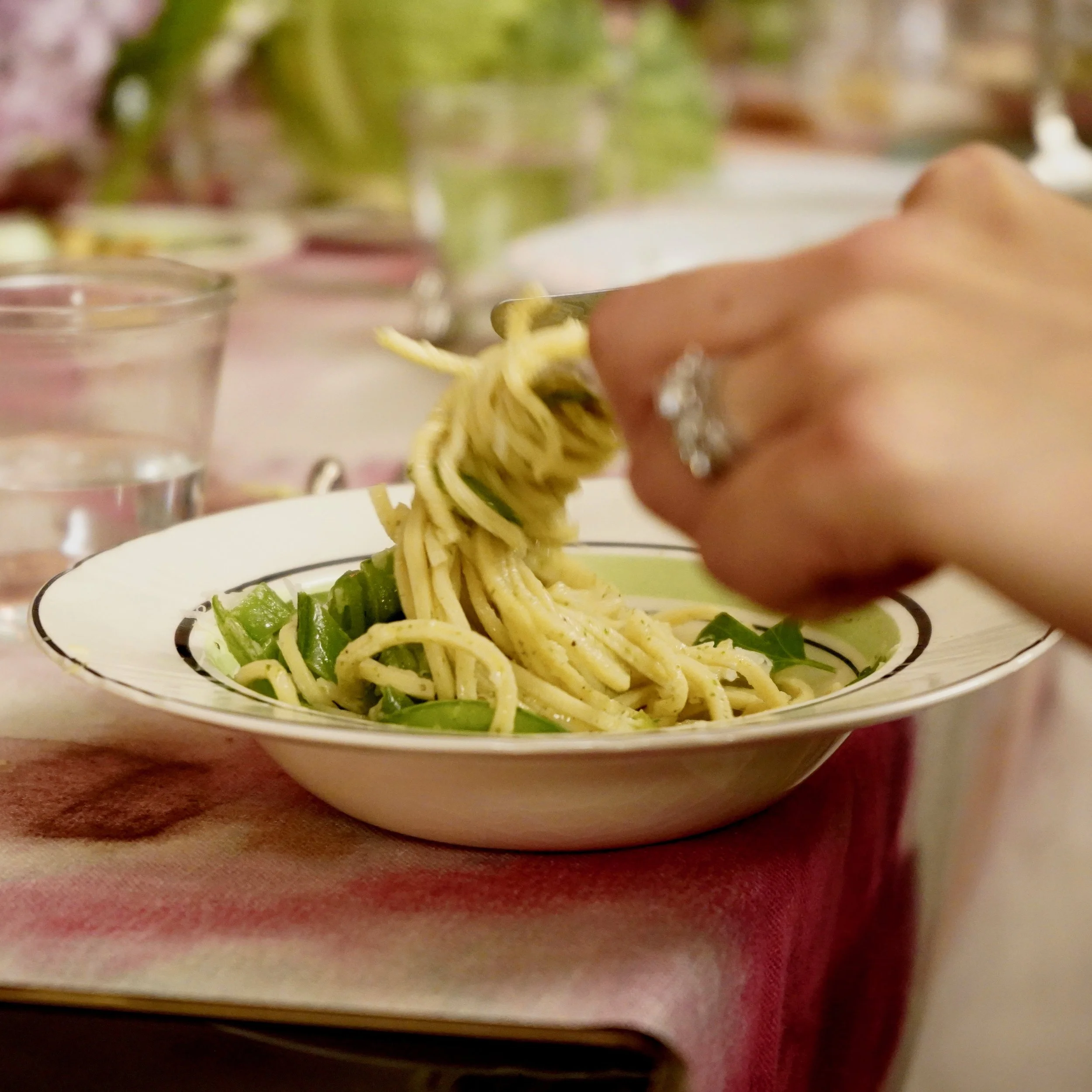 Une main tenant des pâtes avec des légumes dans une assiette sur une table