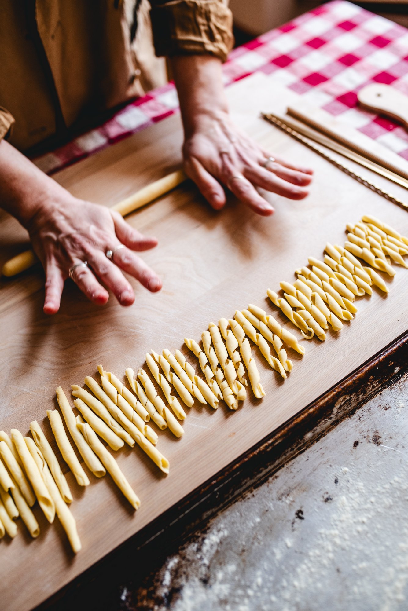 Mains qui façonnent des pâtes fraîches sur un plan de travail en bois.