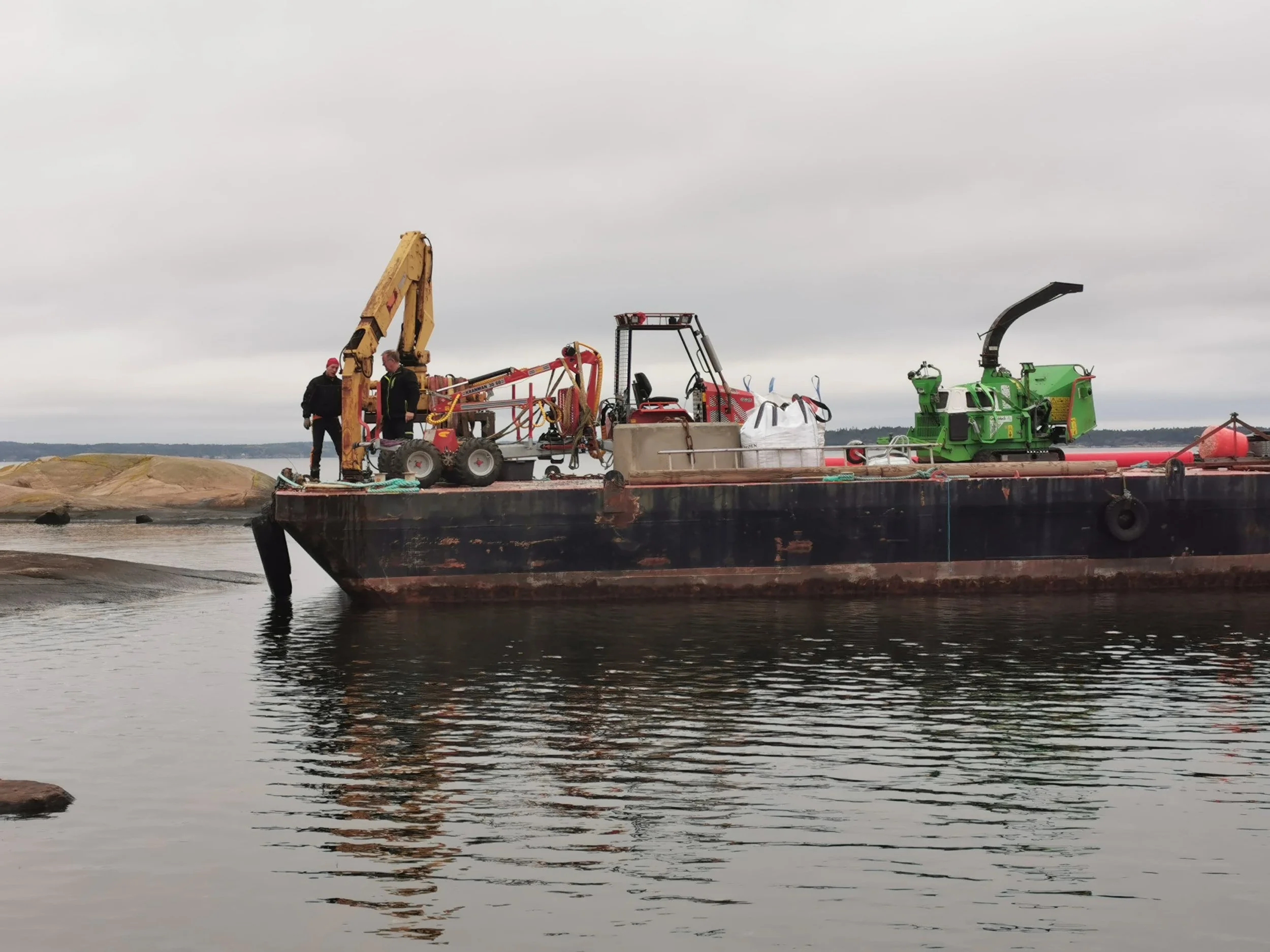 People on a barge using machinery to process rocks or sediment in water under a cloudy sky.