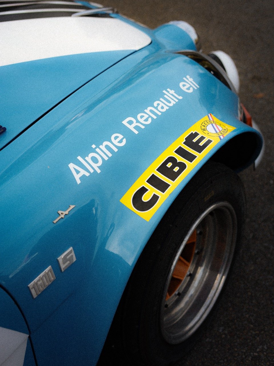 Voiture de course alpine avec stickers, notamment renault, cibie, et d'autres logos, à l'extérieur.