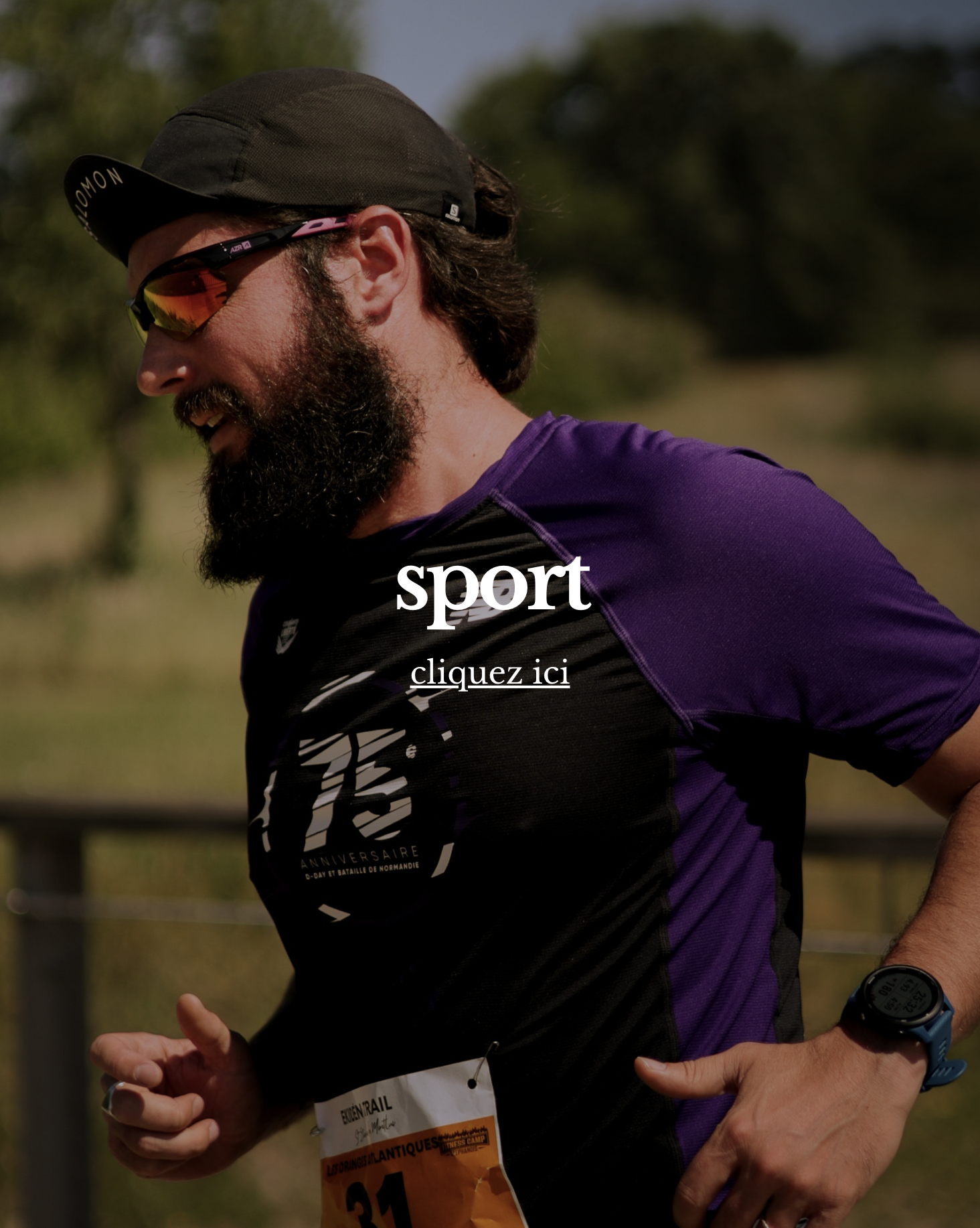 Un homme courant, portant une casquette noire, des lunettes de soleil, un t-shirt de course violet et noir, et une montre de sport, en plein air avec des arbres en arrière-plan