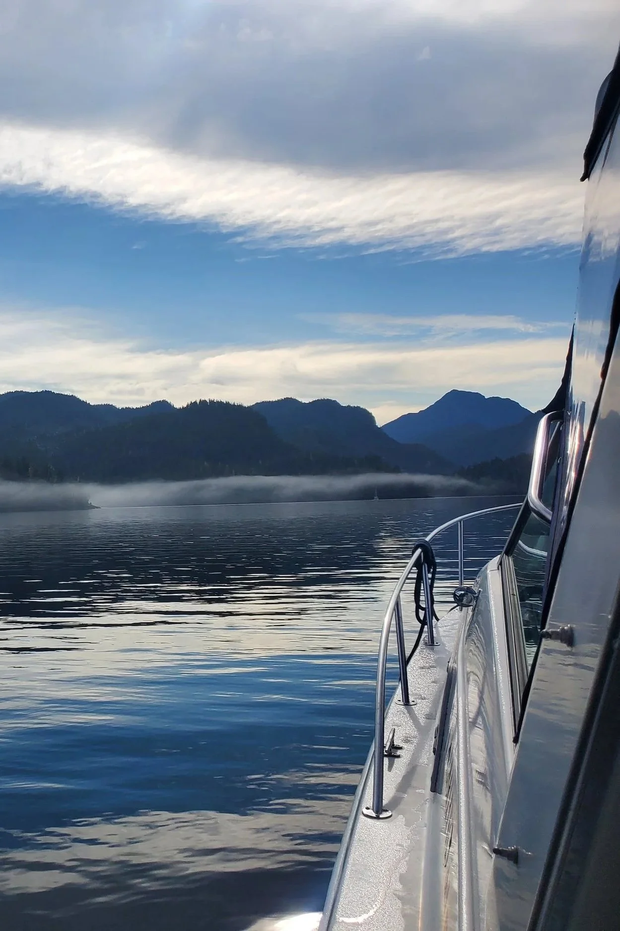 View from a boat on a calm body of water with mountains in the background and a partly cloudy sky.