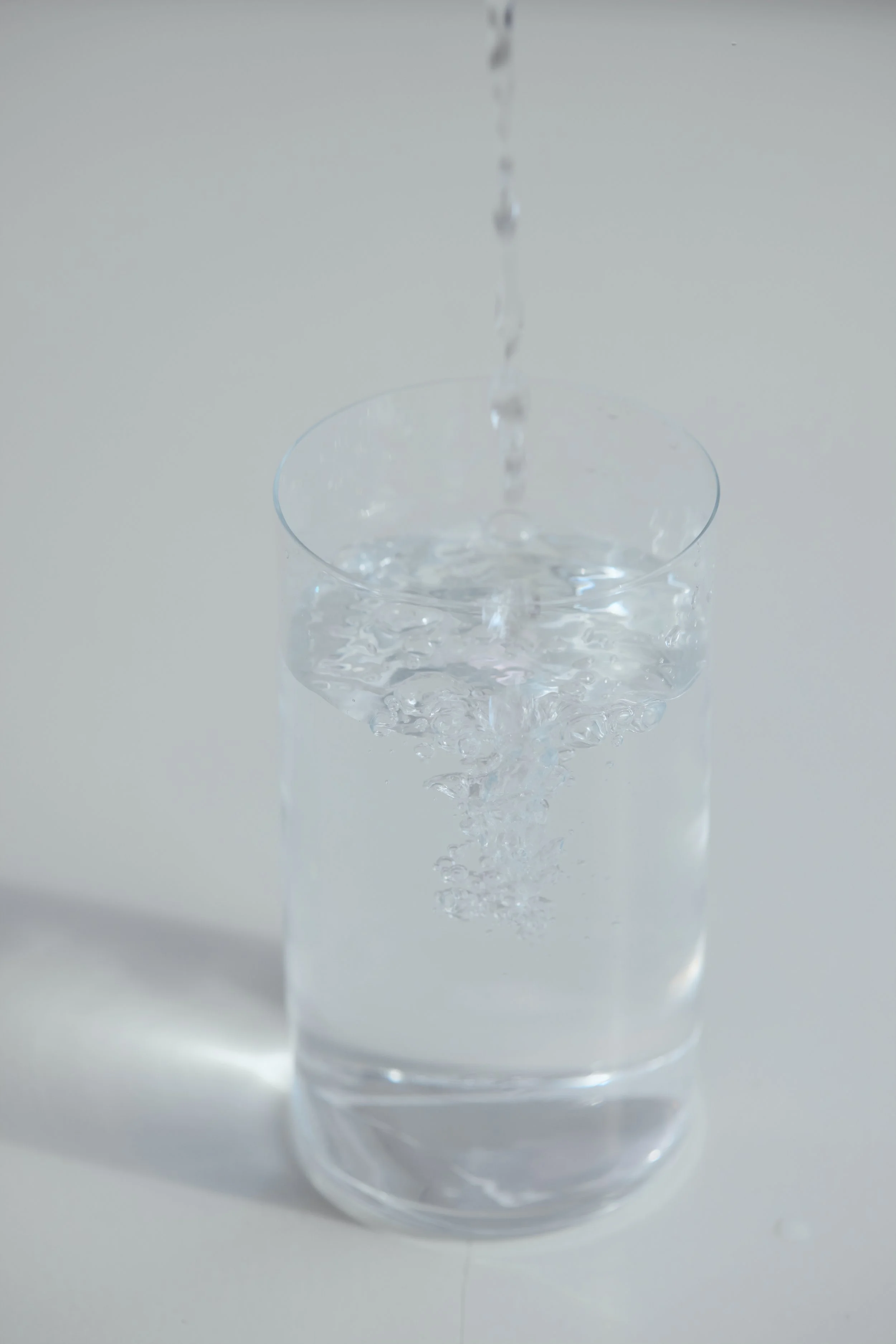 A glass of clear water with a stream of water being poured into it.