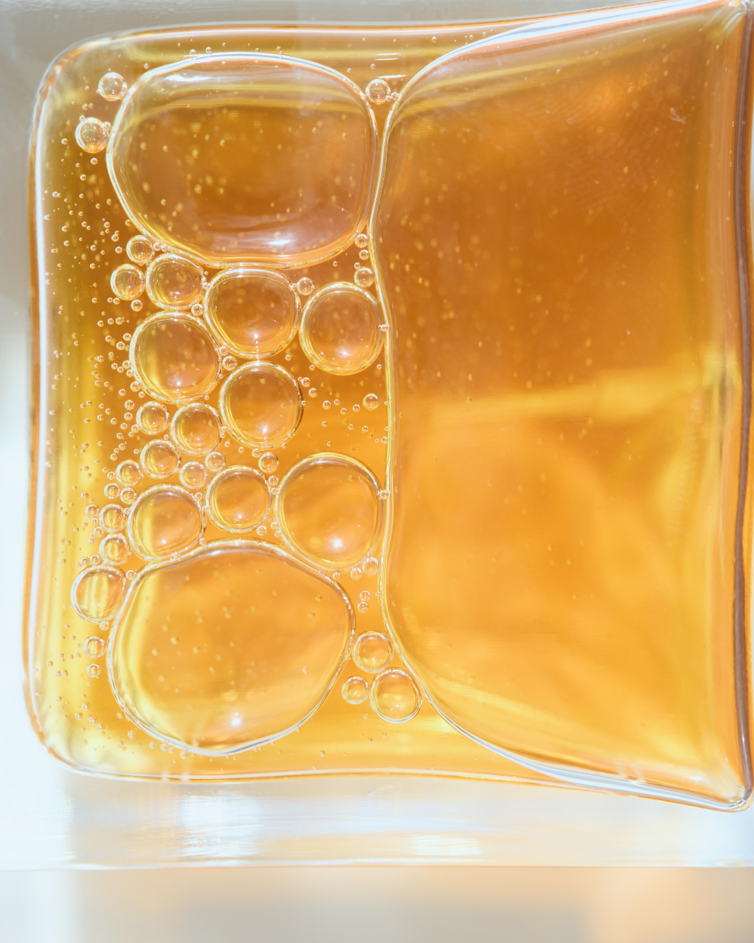 Close-up of golden honey in a square glass container with bubbles.