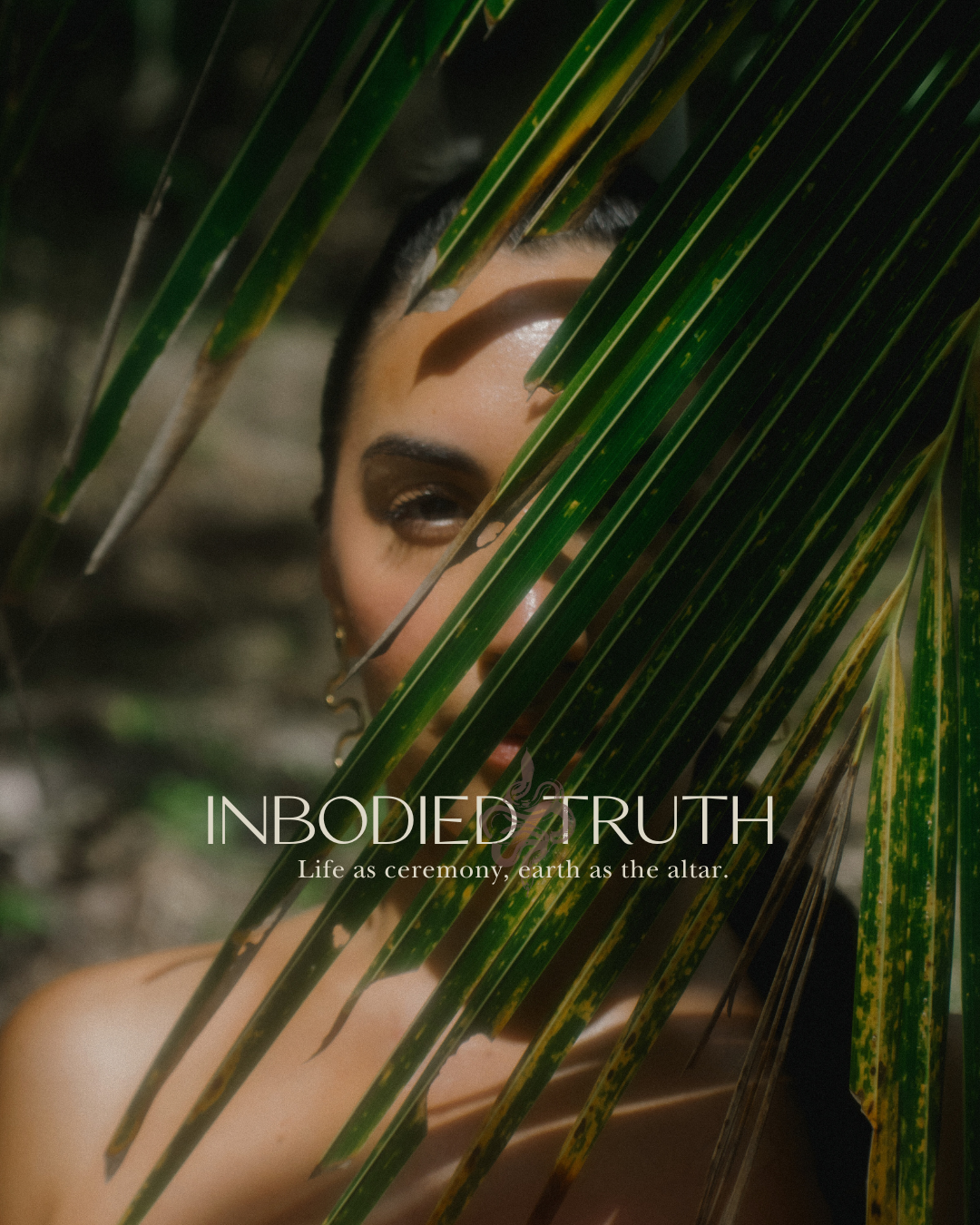 A woman with dark hair and makeup peeking through palm leaves, with text that reads 'INBODIED TRUTH: Life as ceremony, earth as the altar'.