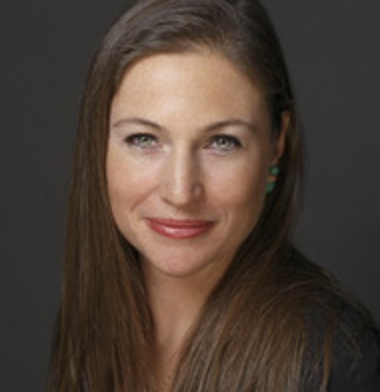 Close-up portrait of a woman with long brown hair and blue eyes, smiling gently against a dark background.