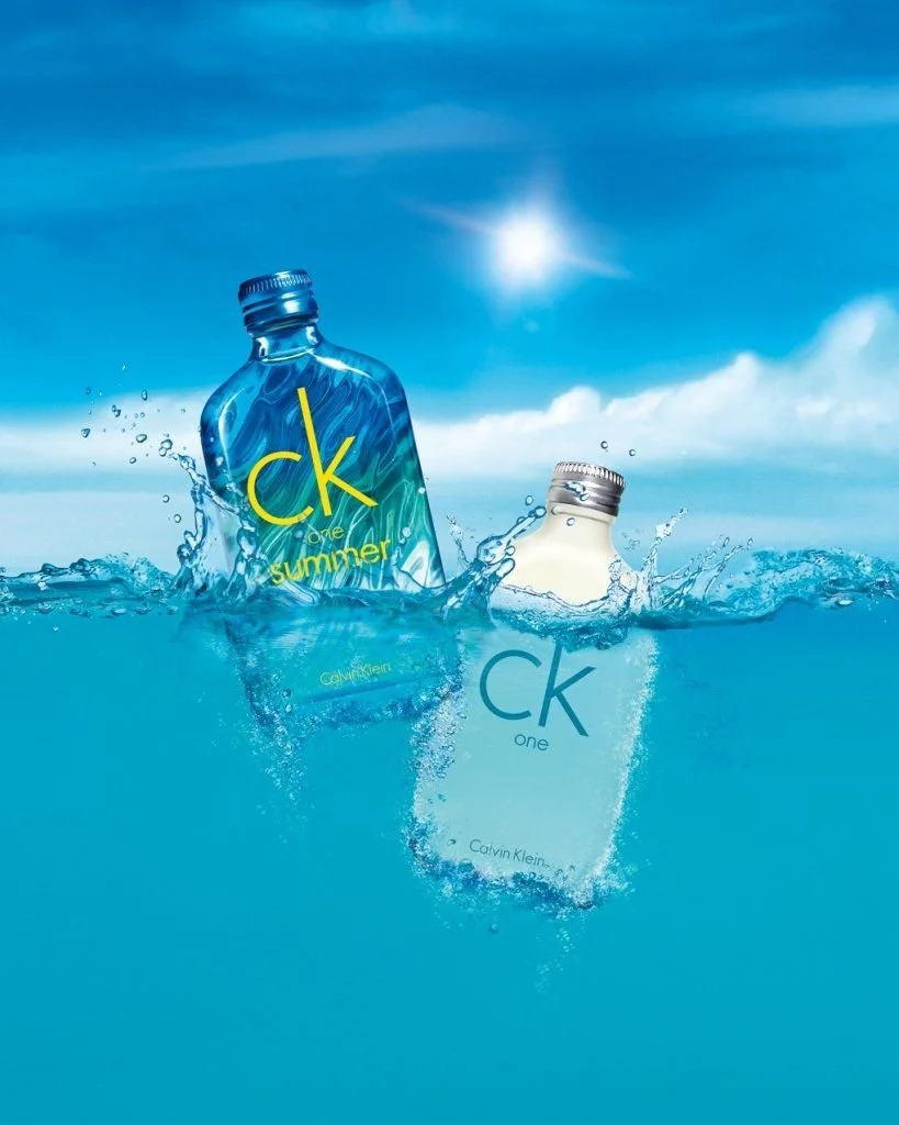 Two bottles of Calvin Klein One fragrance partially submerged in water with a blue sky and sun in the background.