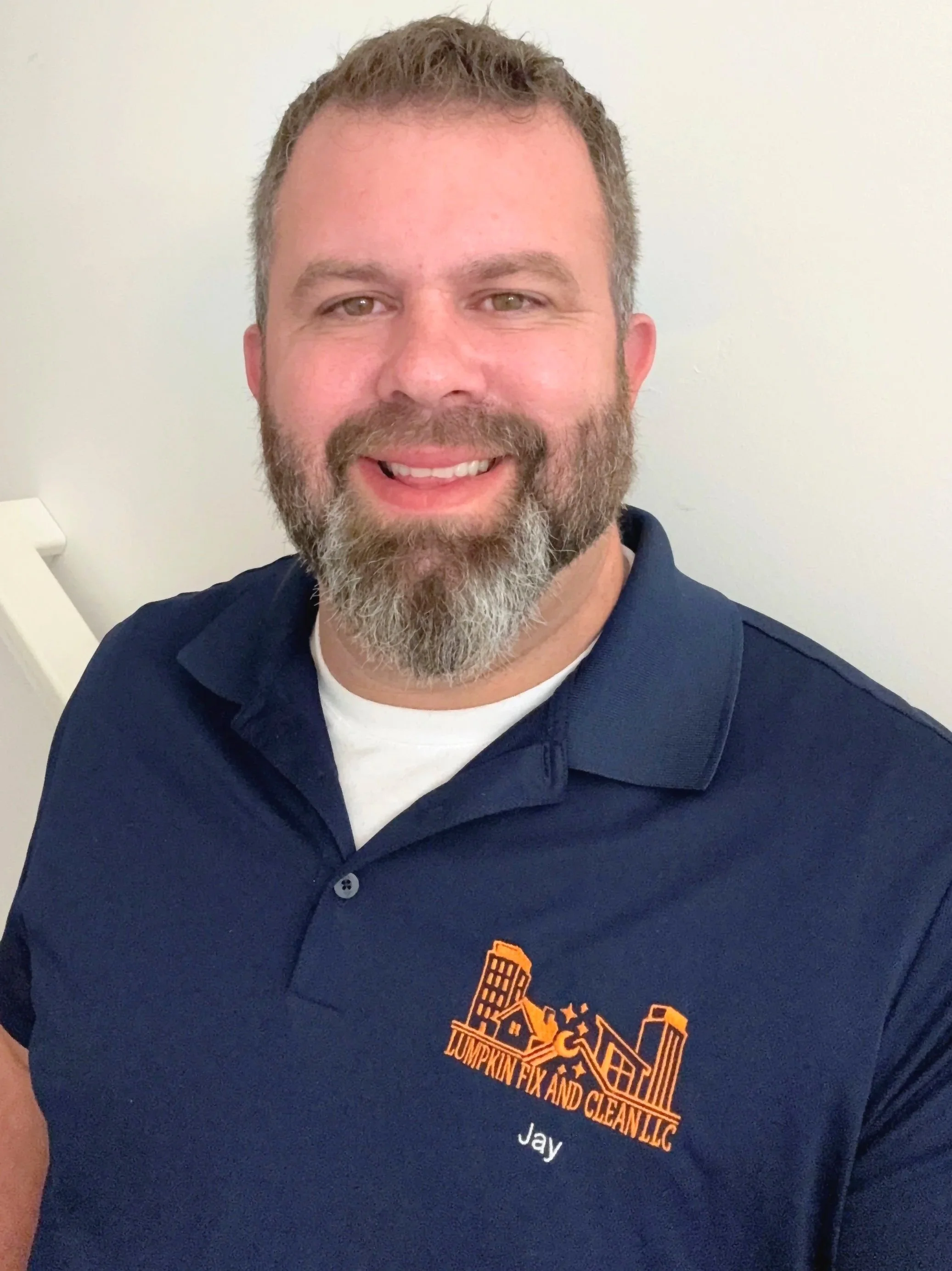 A man with light brown hair and a beard wearing a navy blue quotepumping fix and cleanquot shirt smiling at the camera. The background is plain white.