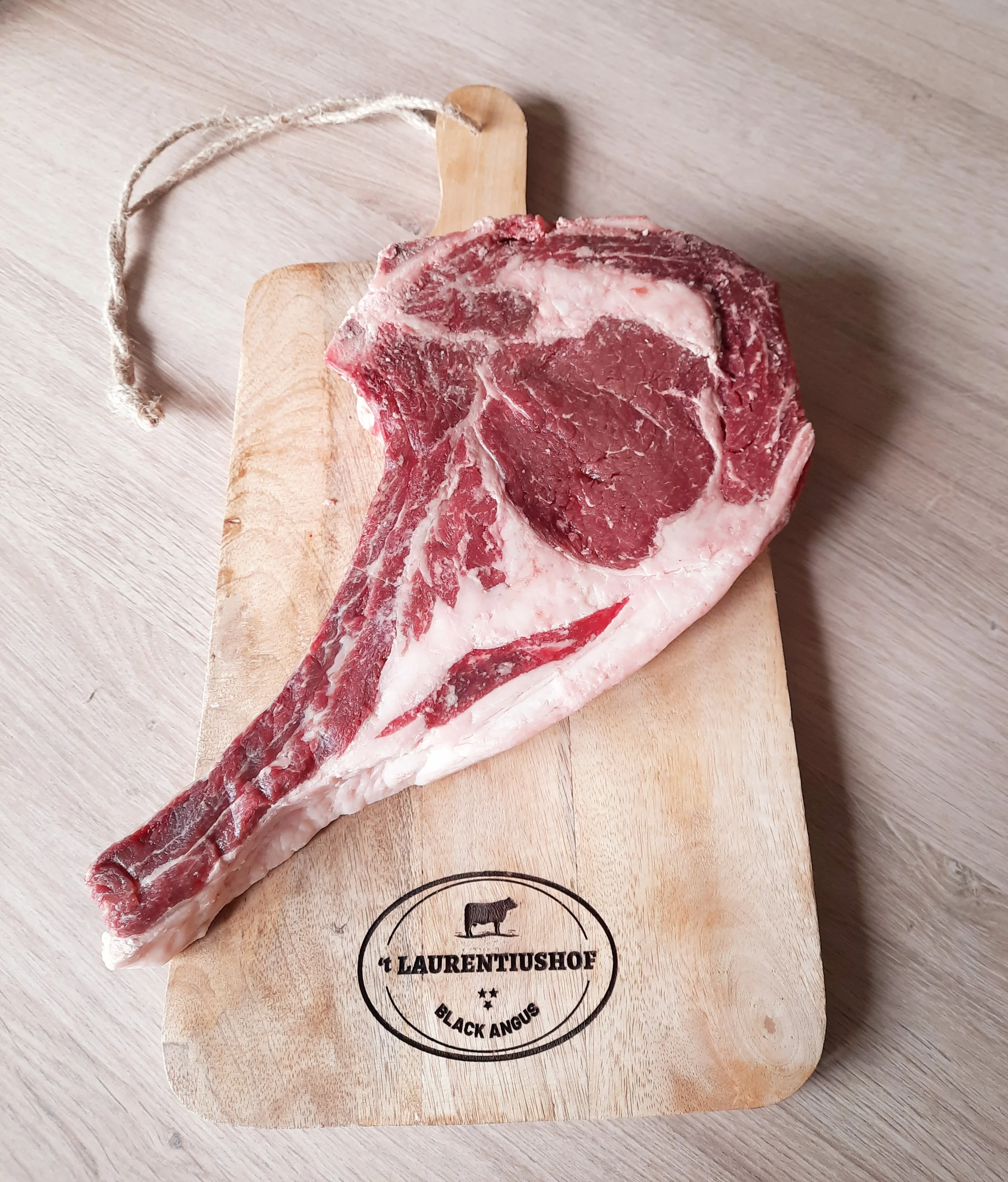 Een groot stuk rauw vlees, waarschijnlijk een ossenhaas of gerelateerde snede, op een houten snijplank met het etiket 't LAURENTUSHOF BLACK ANGUS'.