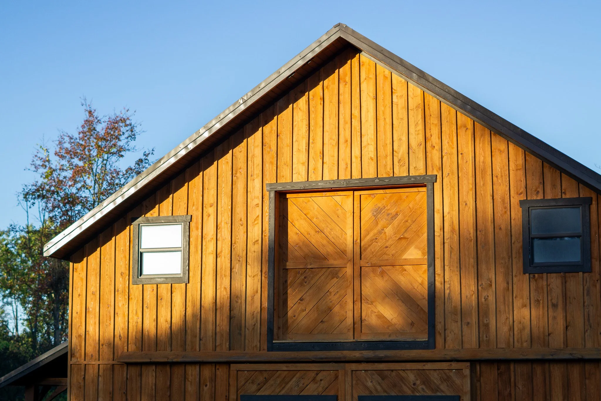 A wooden barn with two small windows and a large sliding door, with sunlight casting shadows on its front.
