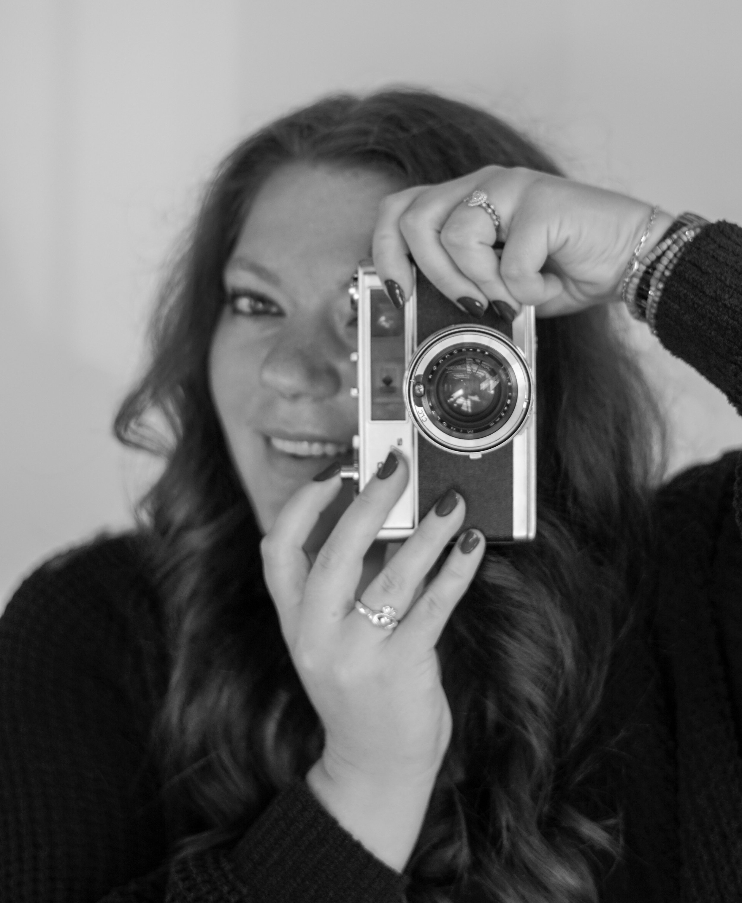 Woman with curly hair taking a selfie with a vintage camera, smiling and looking into the mirror.