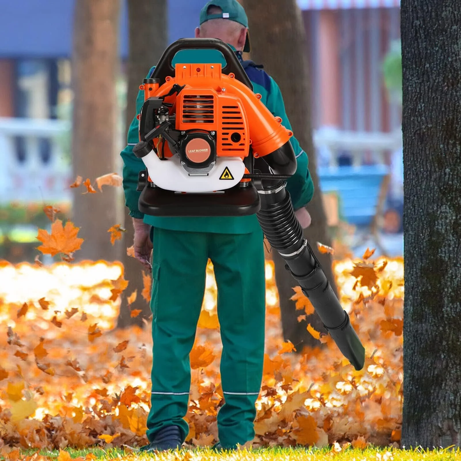 Person in green pants and jacket using a leaf blower to clear fallen autumn leaves in a park.
