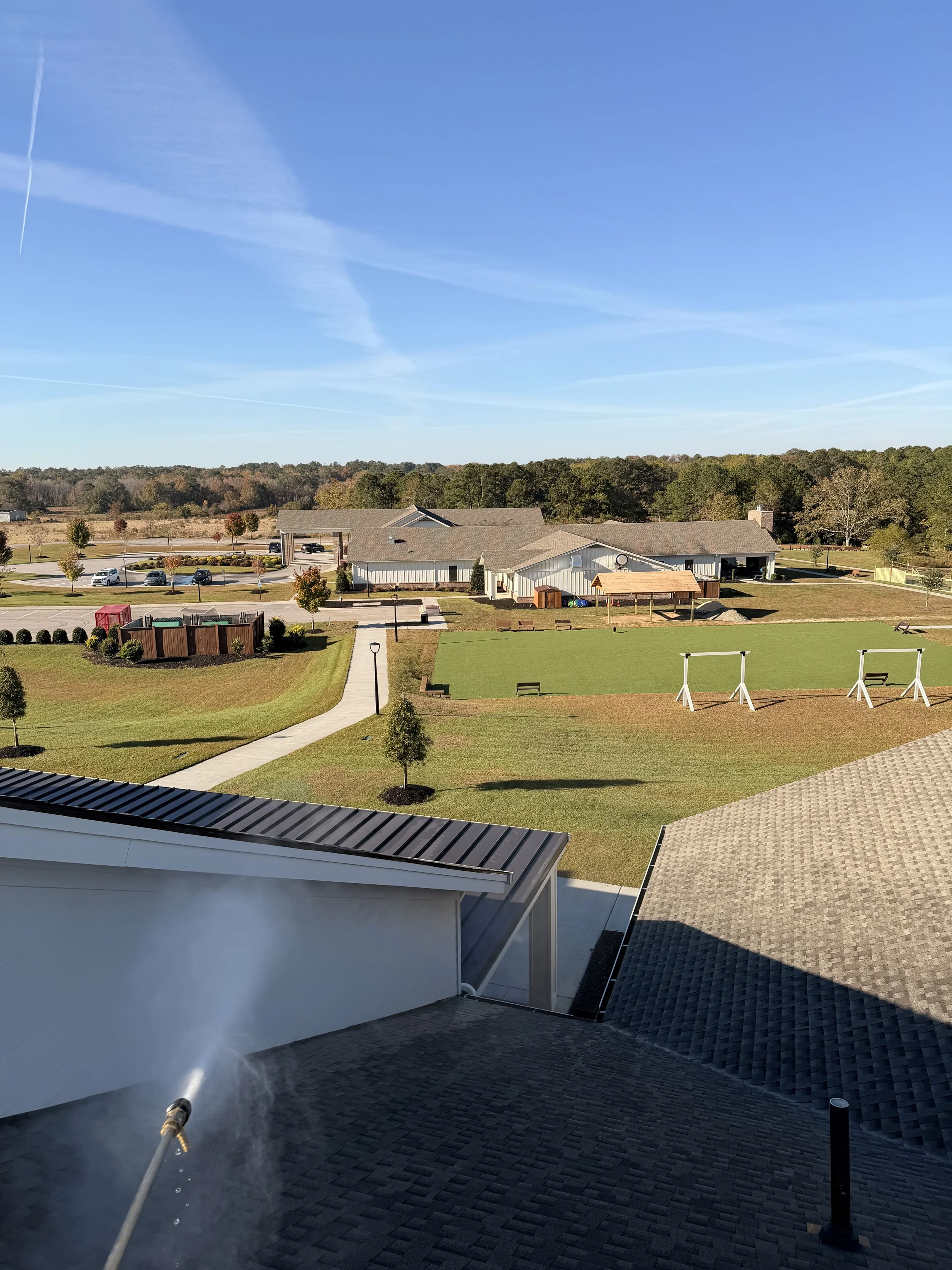 View of a suburban neighborhood with a grassy field, trees, houses, and a blue sky.