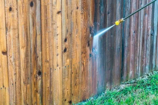 A power washer cleaning a wooden fence with a high-pressure water jet.
