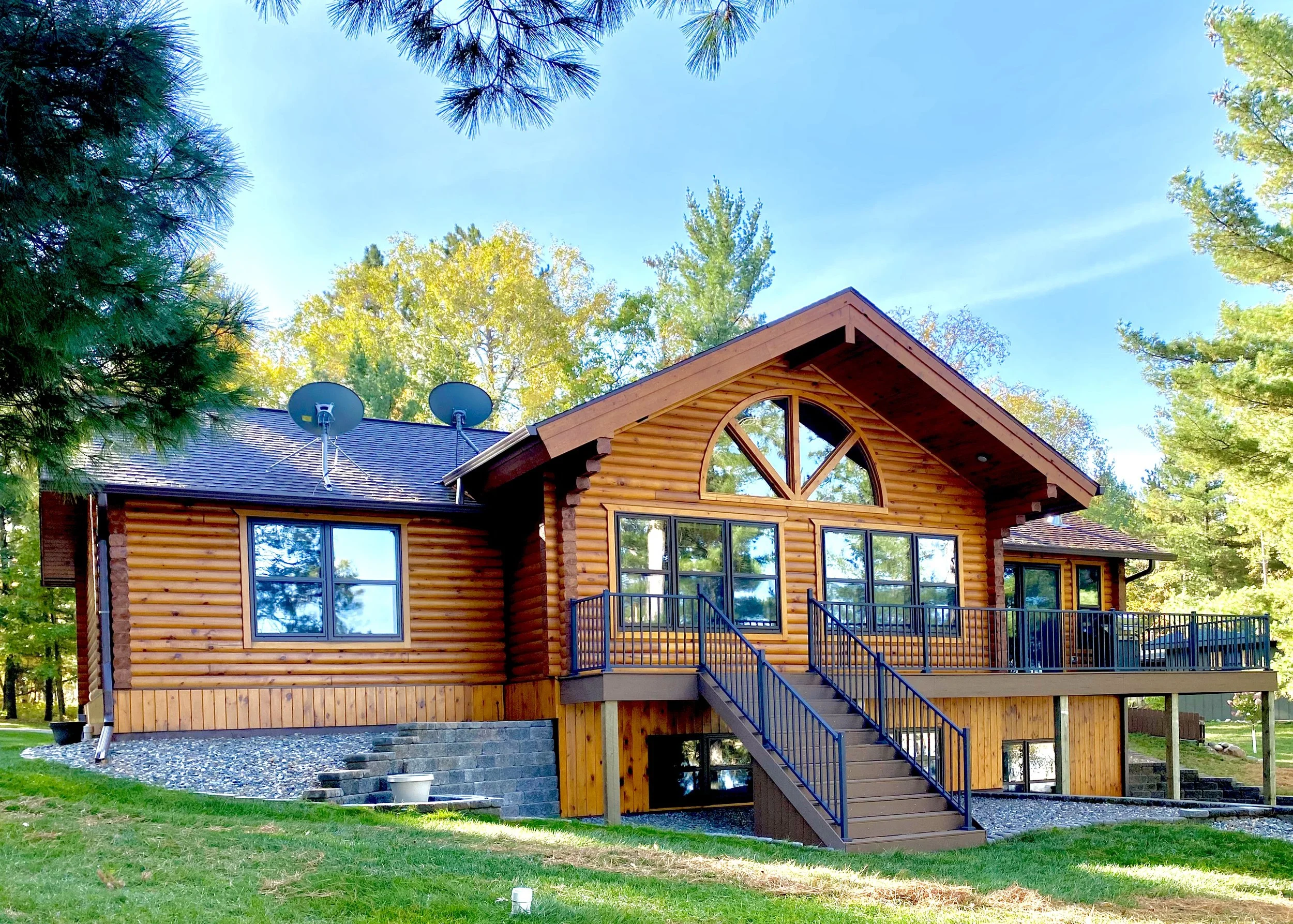 A wooden house with a gabled roof and large front windows, surrounded by trees, with a staircase leading to a front porch.