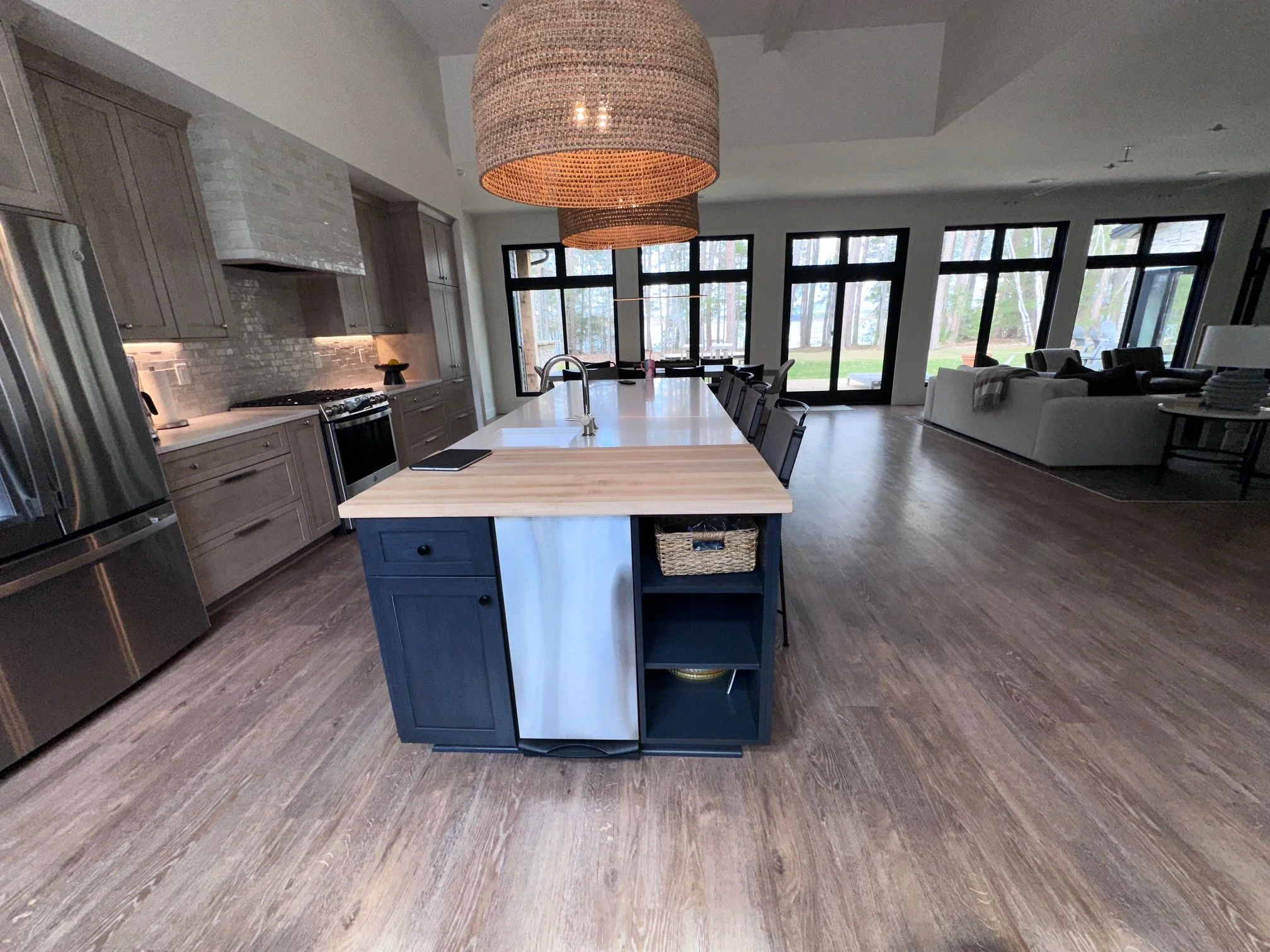 Open-concept kitchen and living room with large island, modern cabinetry, stainless steel appliances, and floor-to-ceiling windows with outdoor views.