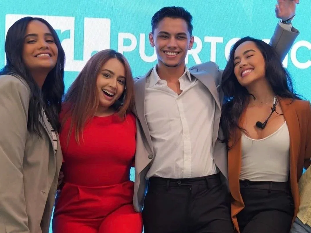 Group of four diverse young adults smiling and posing together at an event with a blue background.