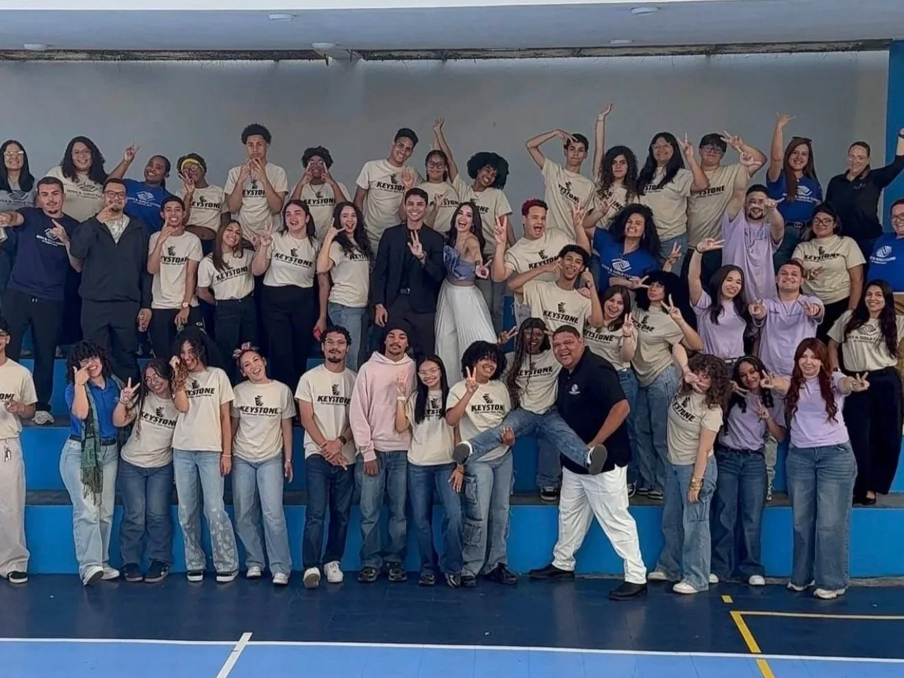 Group of young people and some adults posing for a group photo in a gymnasium or indoor sports facility, with some wearing matching T-shirts with the word 'KESTONE' on them.