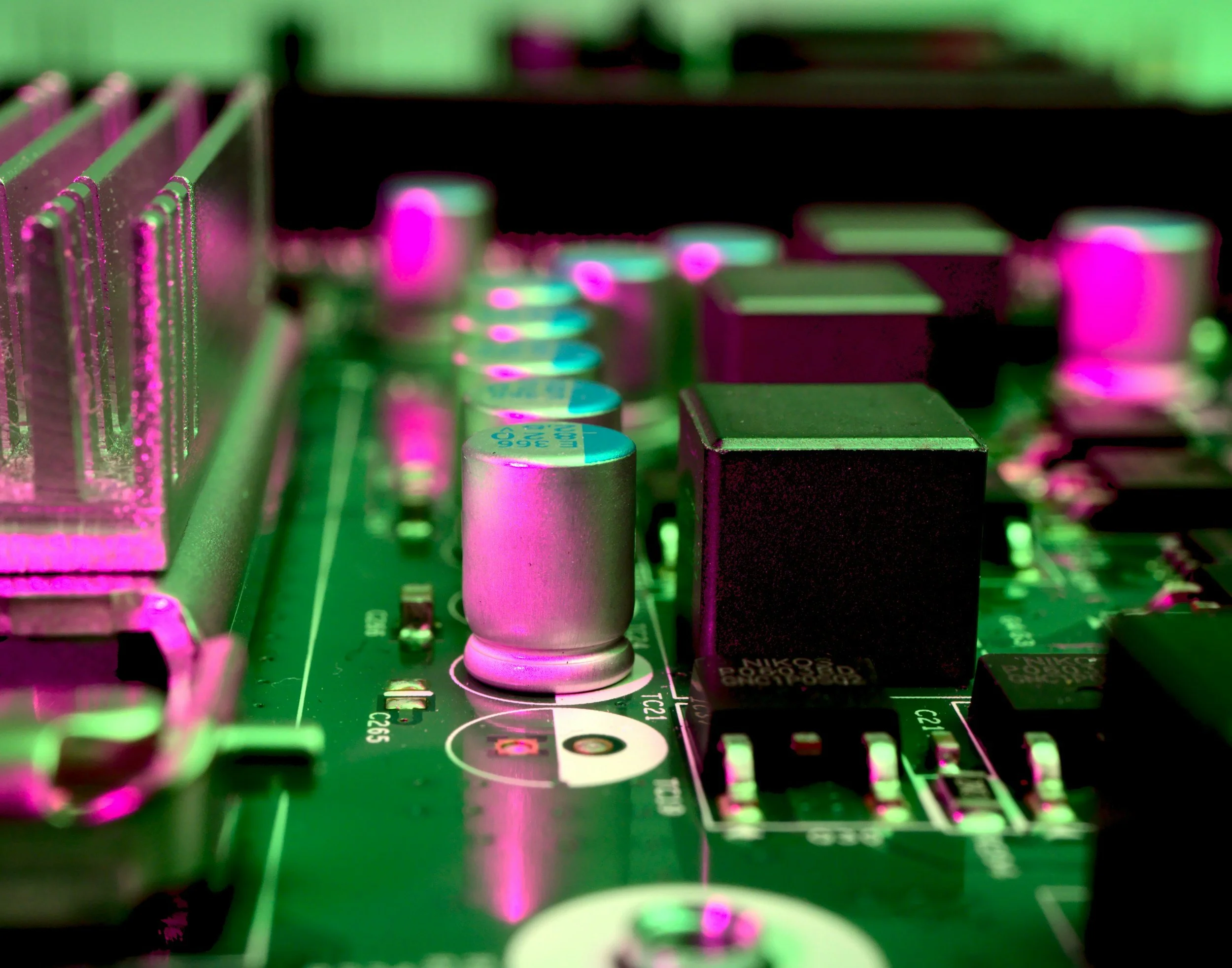 Close-up of a computer motherboard with capacitors and other electronic components under colored lighting.