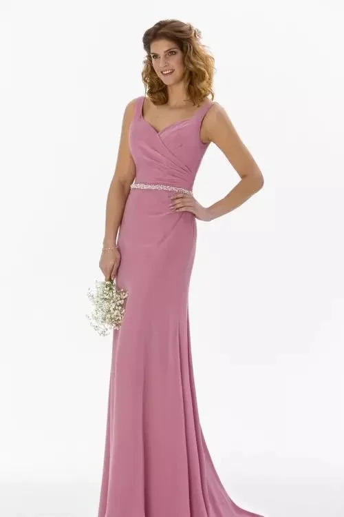 Woman in pink formal gown holding a small bouquet of white flowers, standing against a white background.