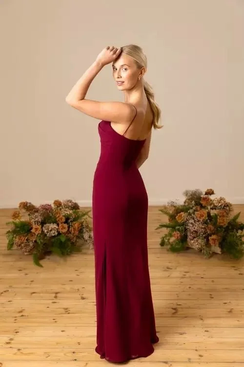A woman in a long, strapless maroon dress standing on a wooden floor with floral arrangements in the background.