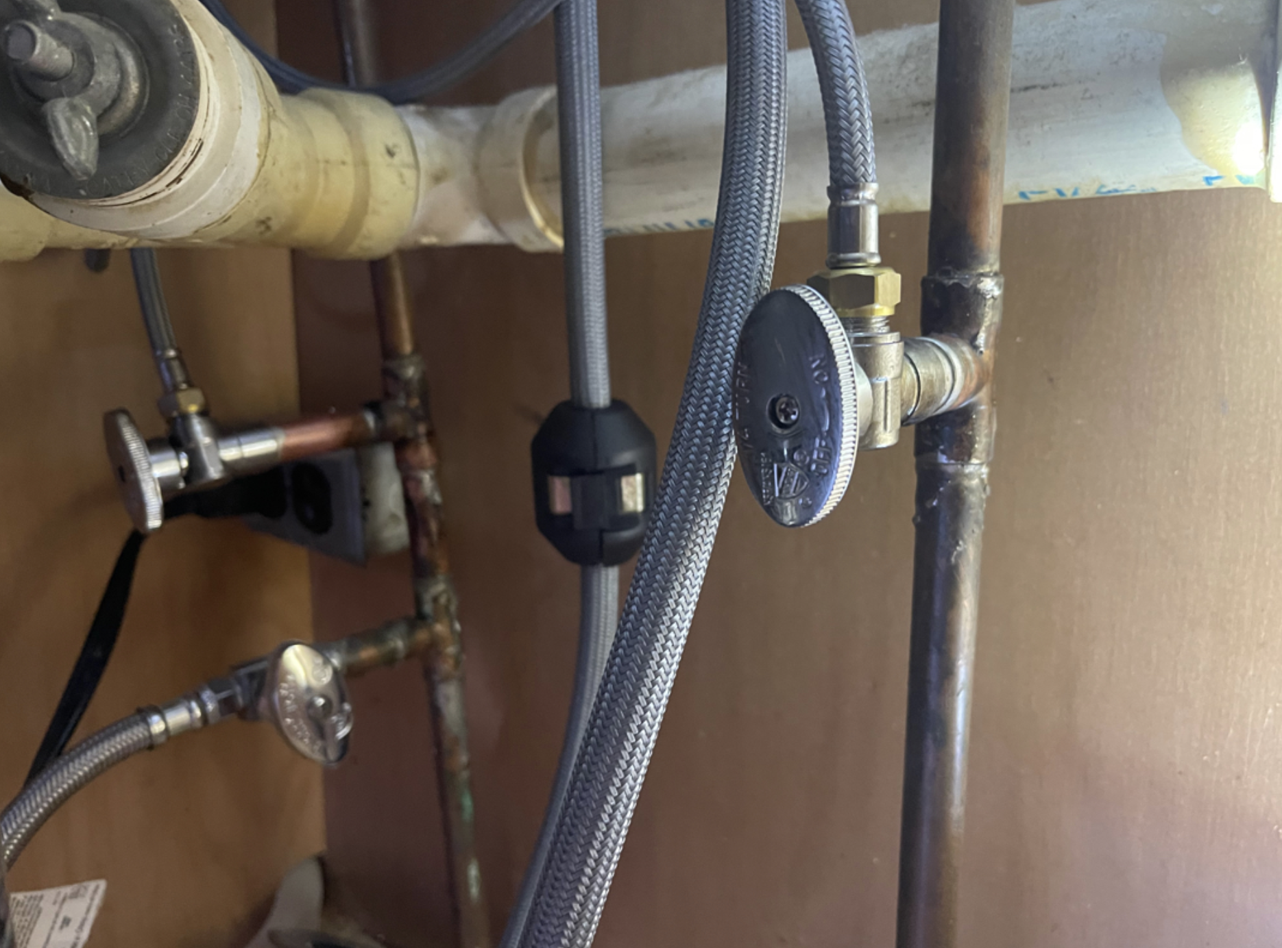 Close-up of plumbing pipes with various valves, fittings, and braided hoses connected to a water supply system.