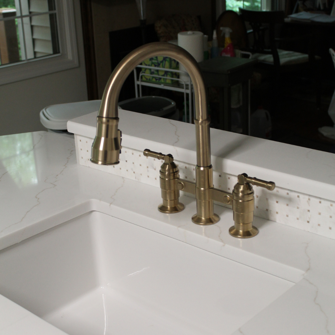 A kitchen sink with a gold-colored faucet and handles on a white marble countertop.