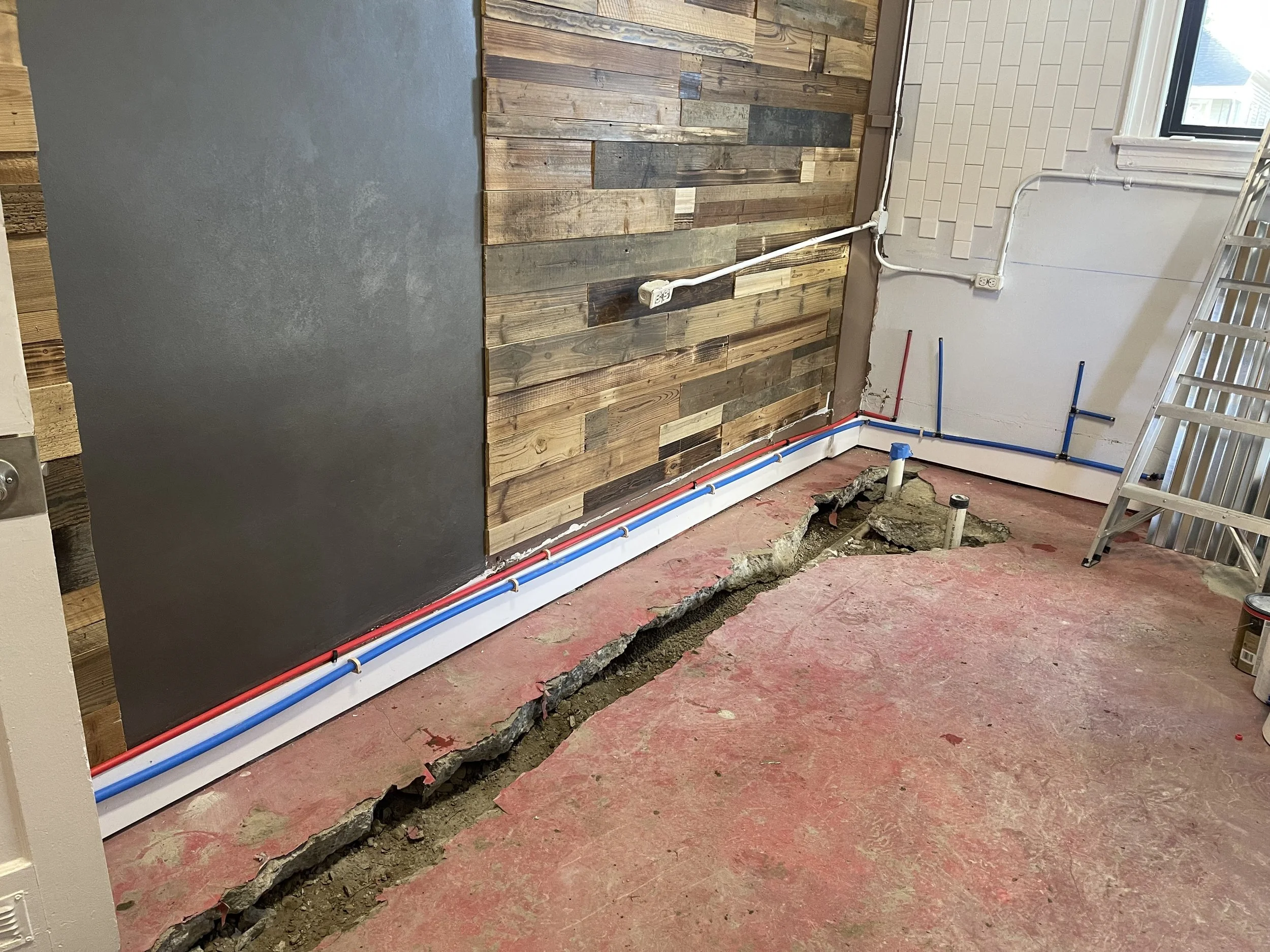 Room under renovation with exposed wiring, a trench in the red concrete floor, and partially finished wooden and painted wall.