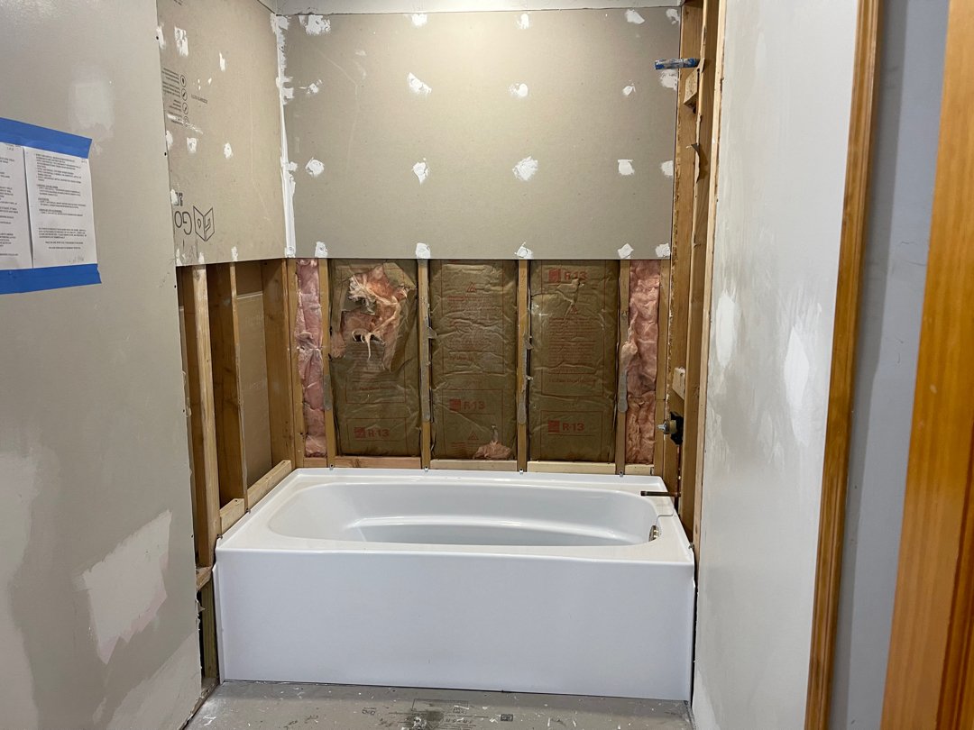 Bathroom under renovation with a partially installed bathtub, exposed insulation, and unfinished drywall.